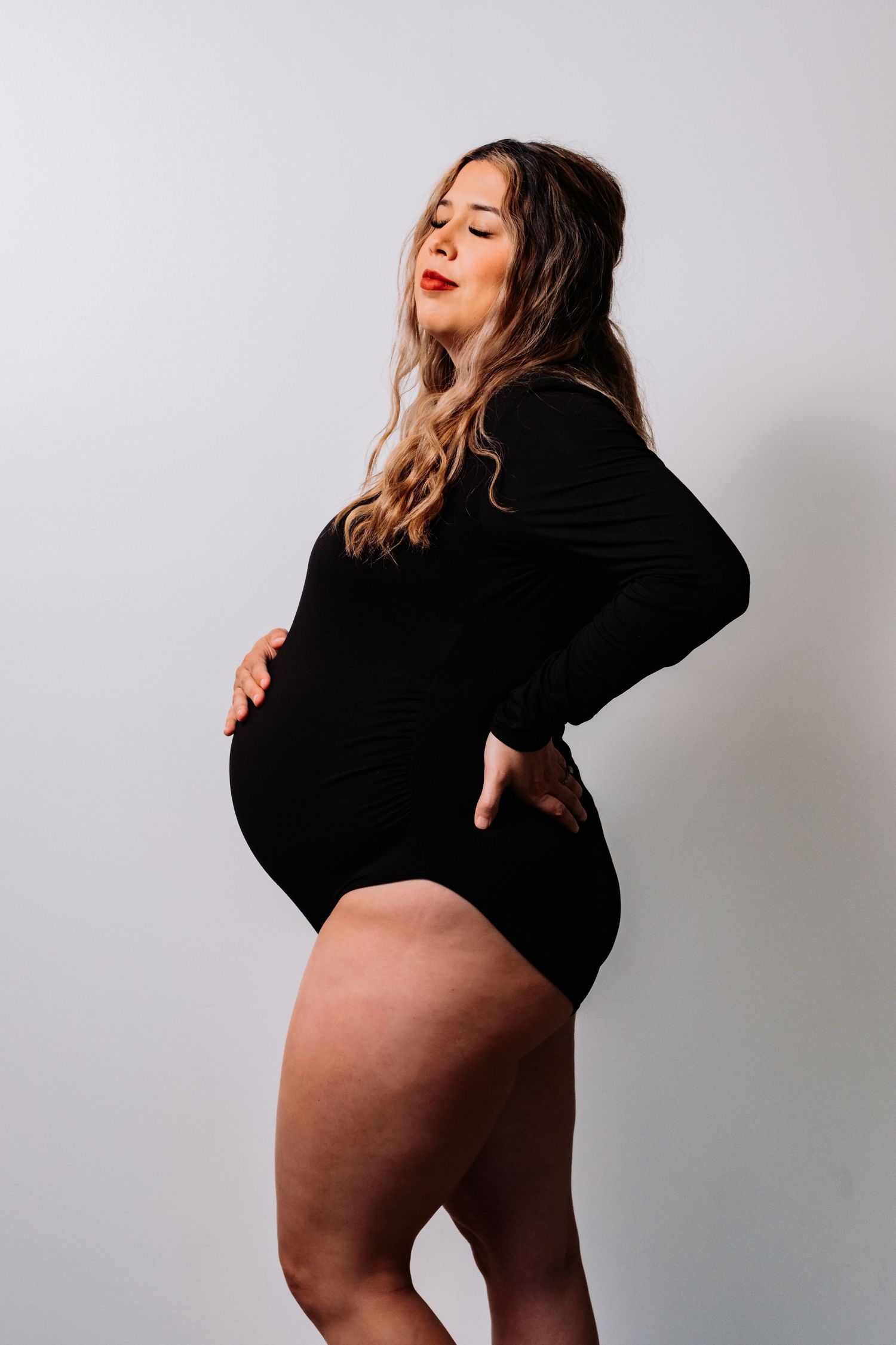 Side profile maternity photo of woman in black bodysuit showing pregnancy silhouette.