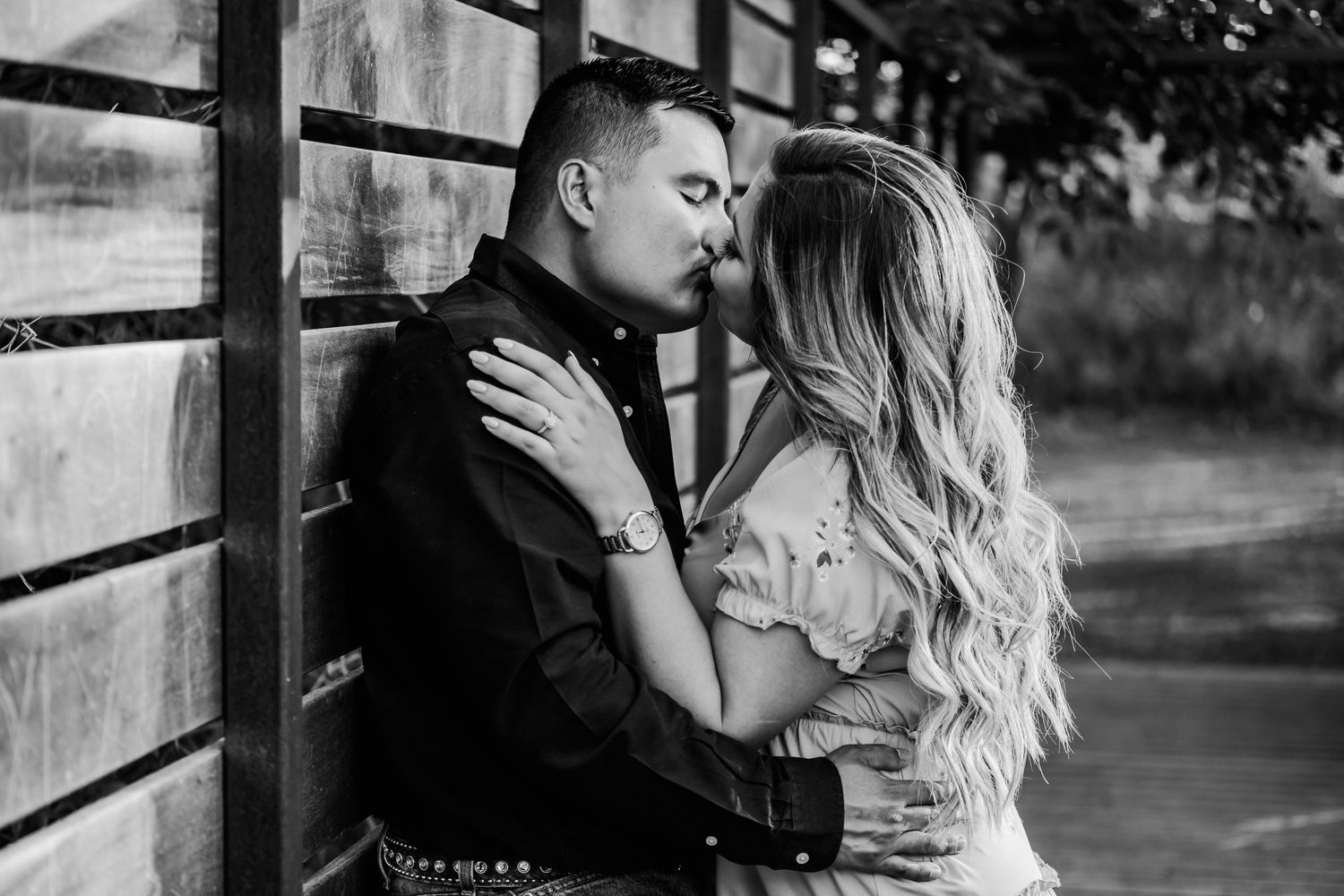 Romantic black and white photo of couple embracing against rustic wooden fence.
