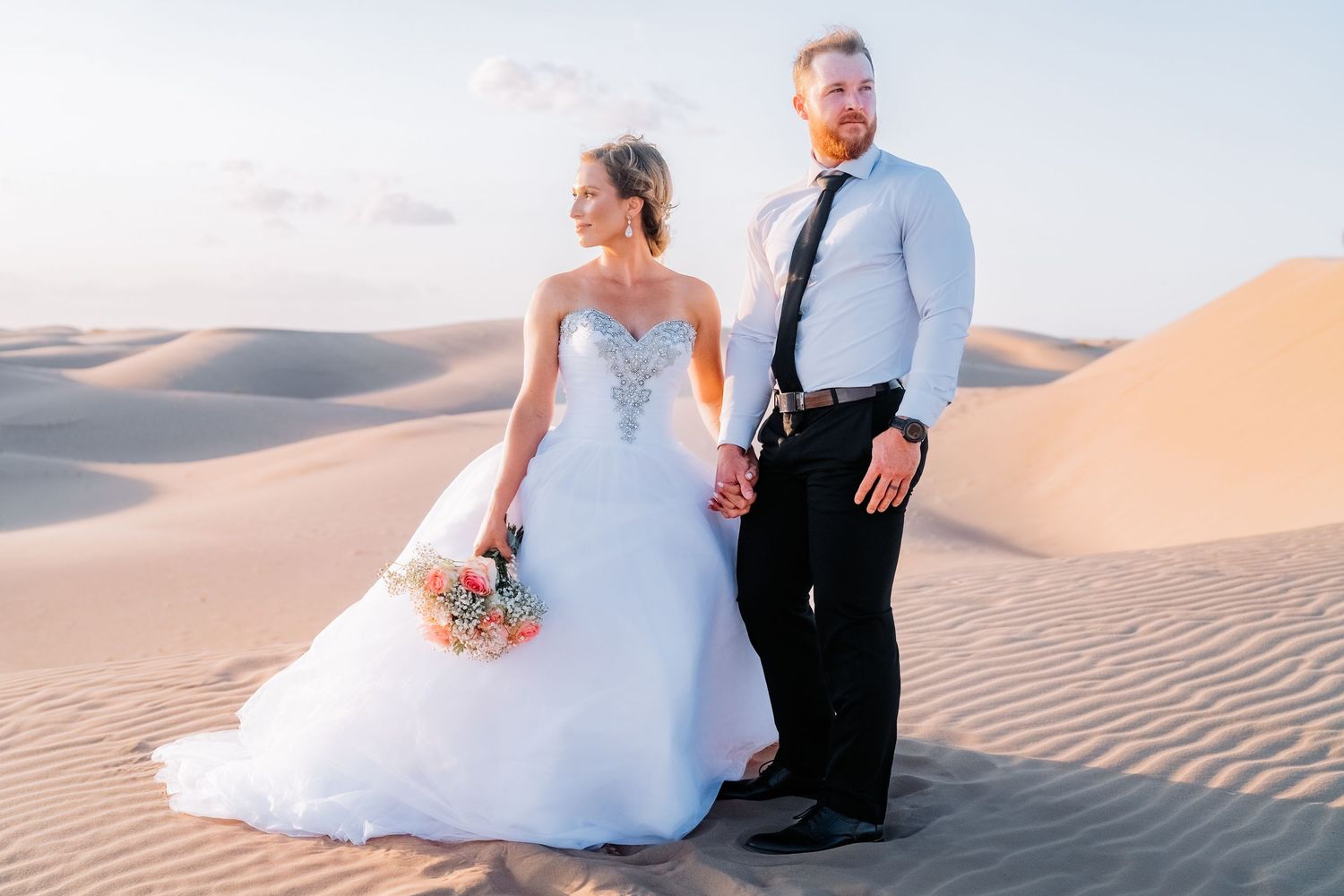 Romantic desert wedding photography featuring a couple amid golden sand dunes at dusk.