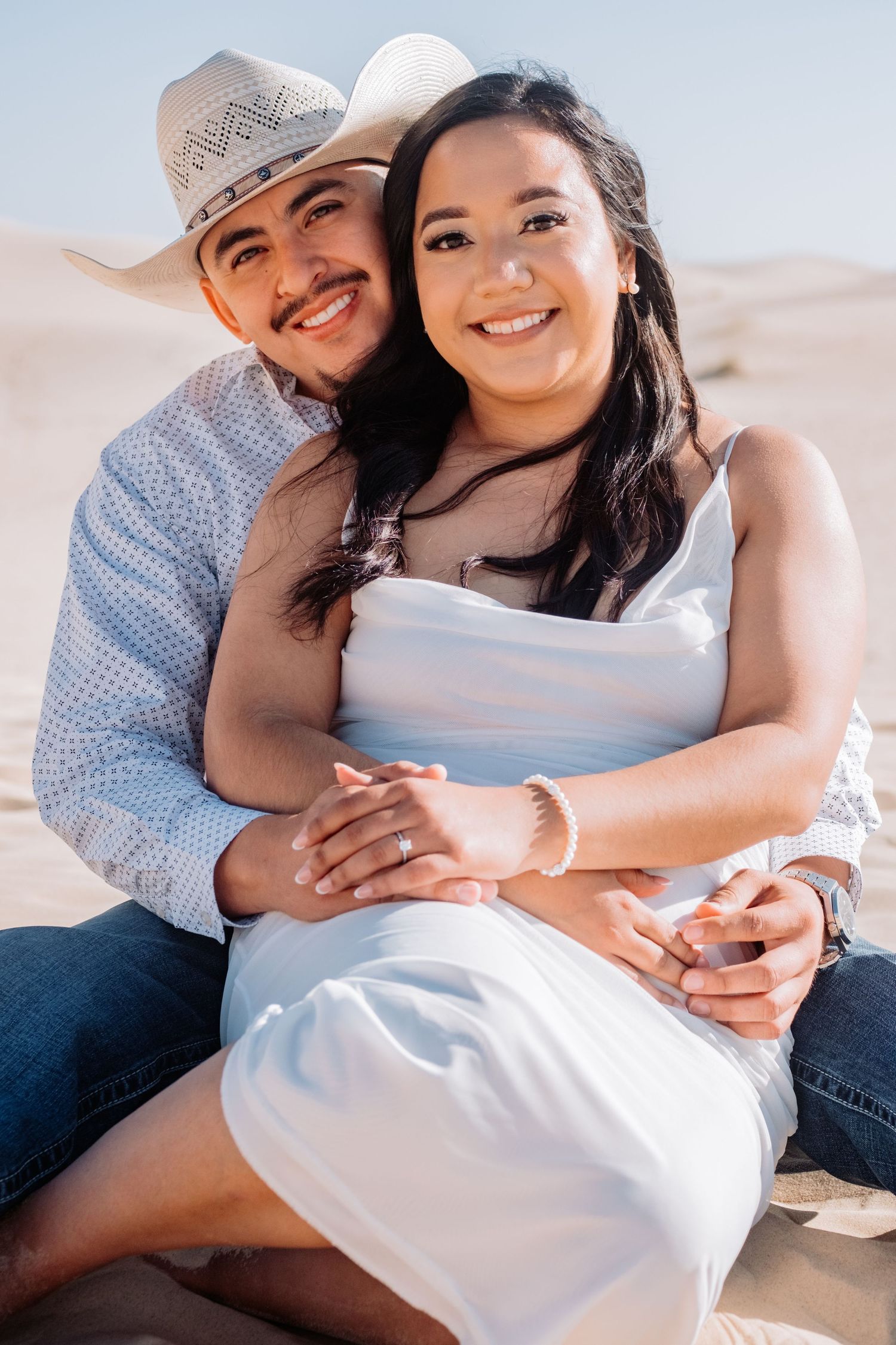 Romantic couple poses lovingly together on sandy beach during sunset photoshoot.