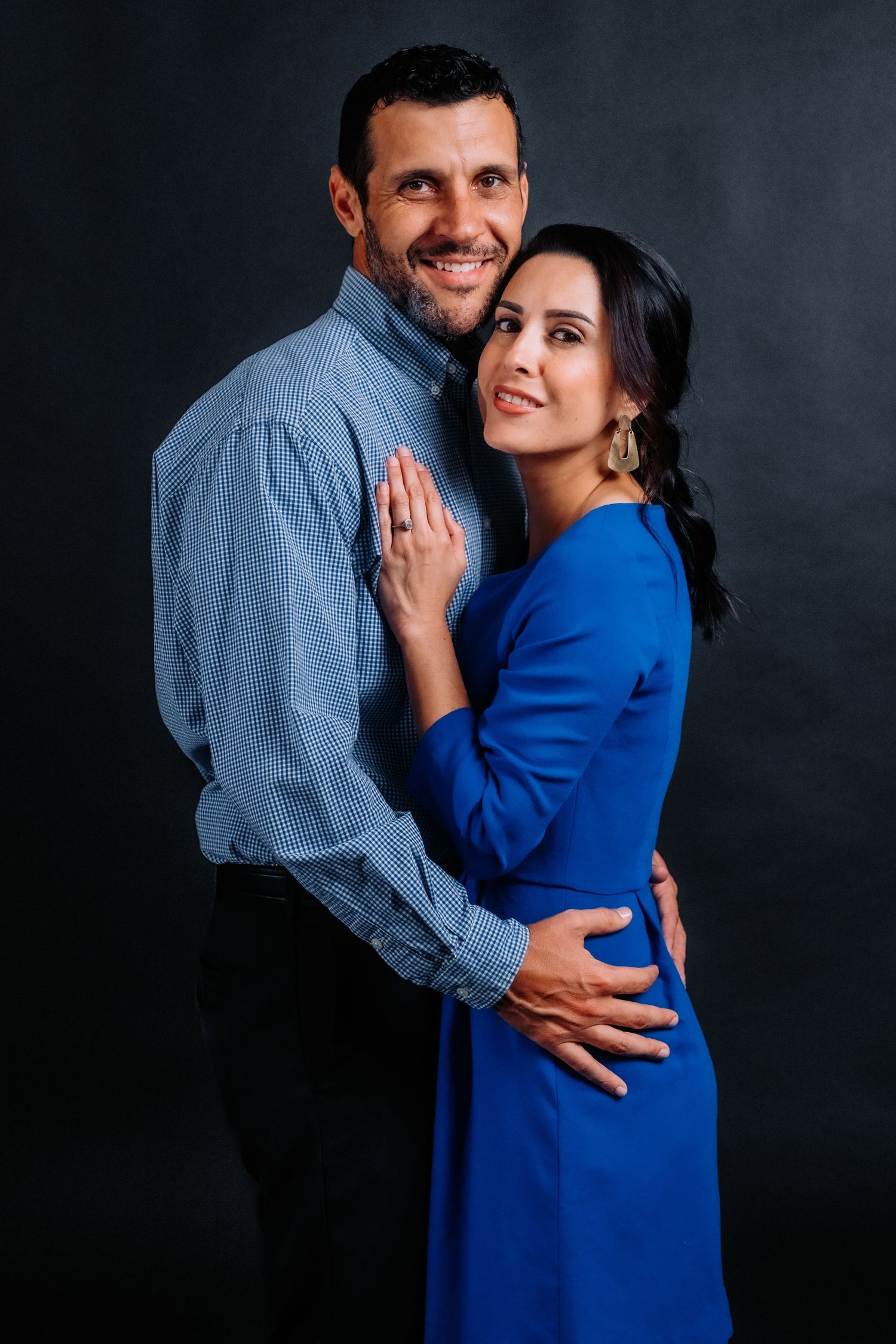 Romantic studio portrait of couple in blue attire embracing against black backdrop.