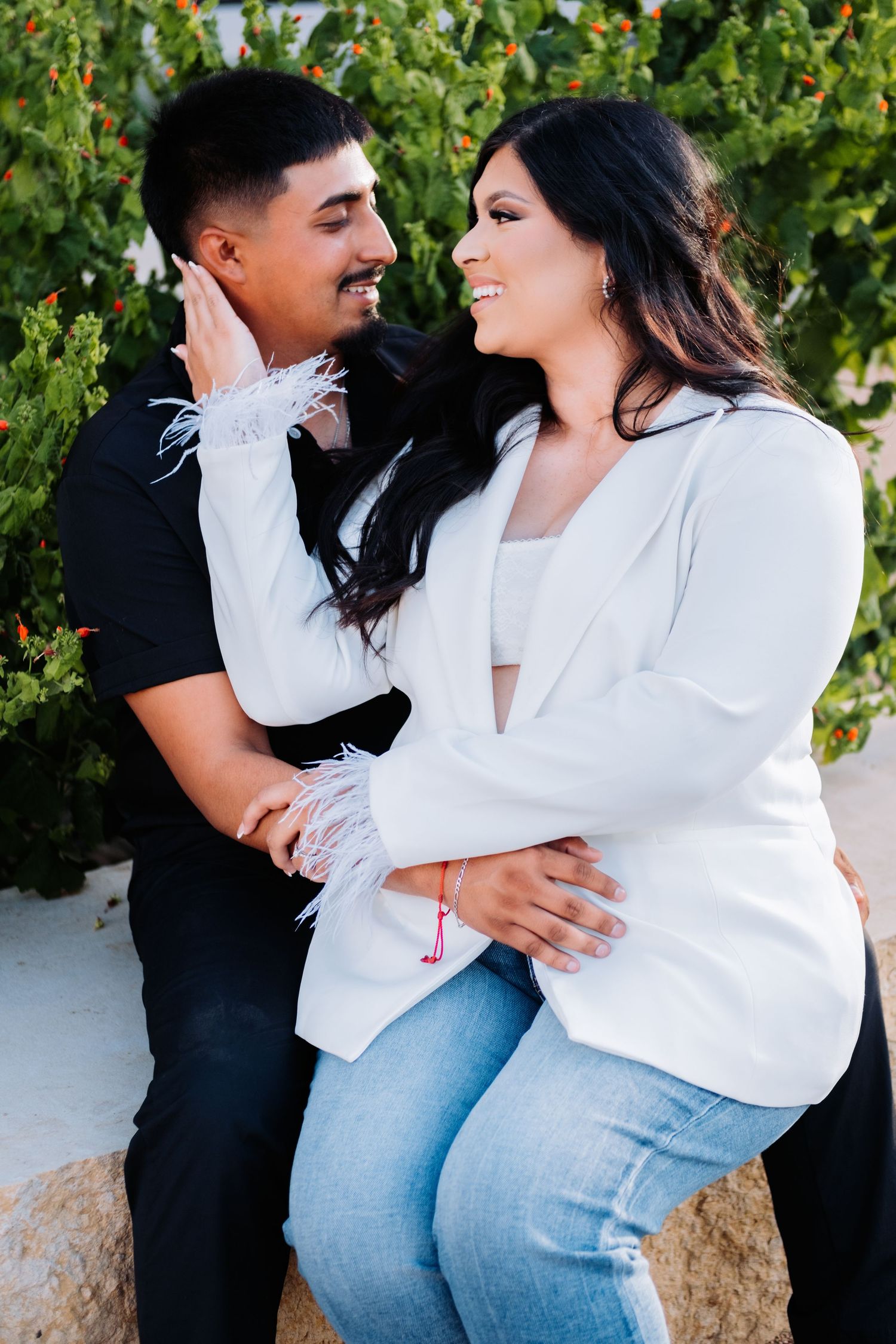 A couple in casual attire poses playfully against a green garden backdrop.