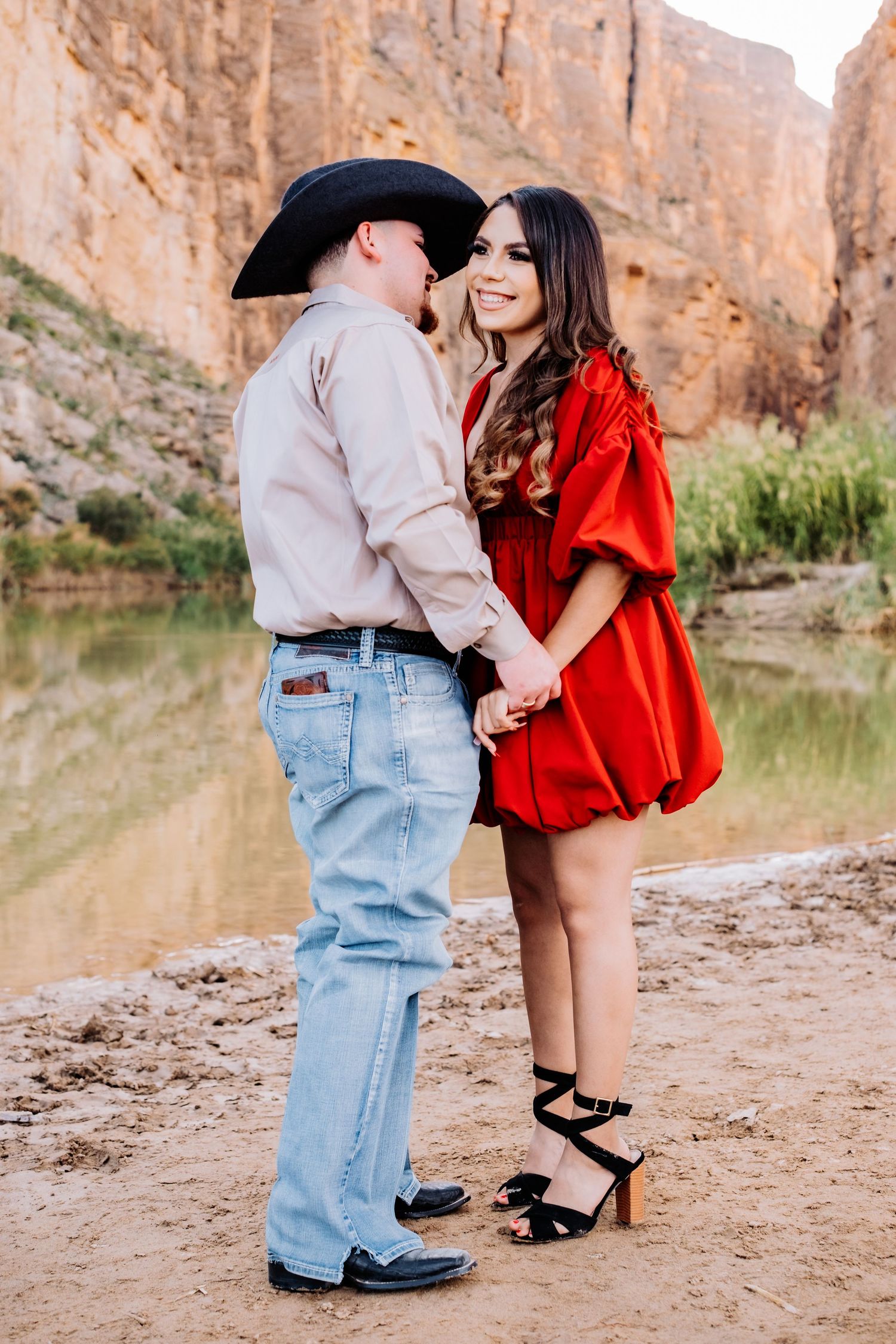 A couple poses playfully near red canyon walls and a water feature.