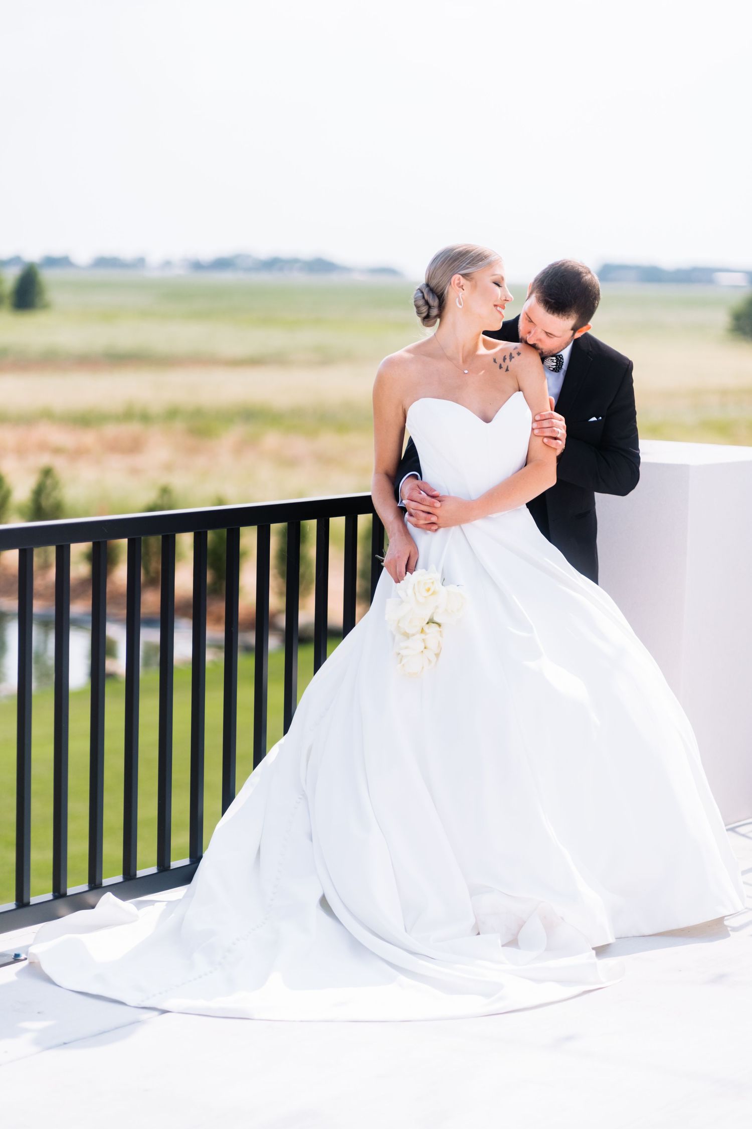 A romantic couple share an intimate moment on a balcony in elegant wedding attire.