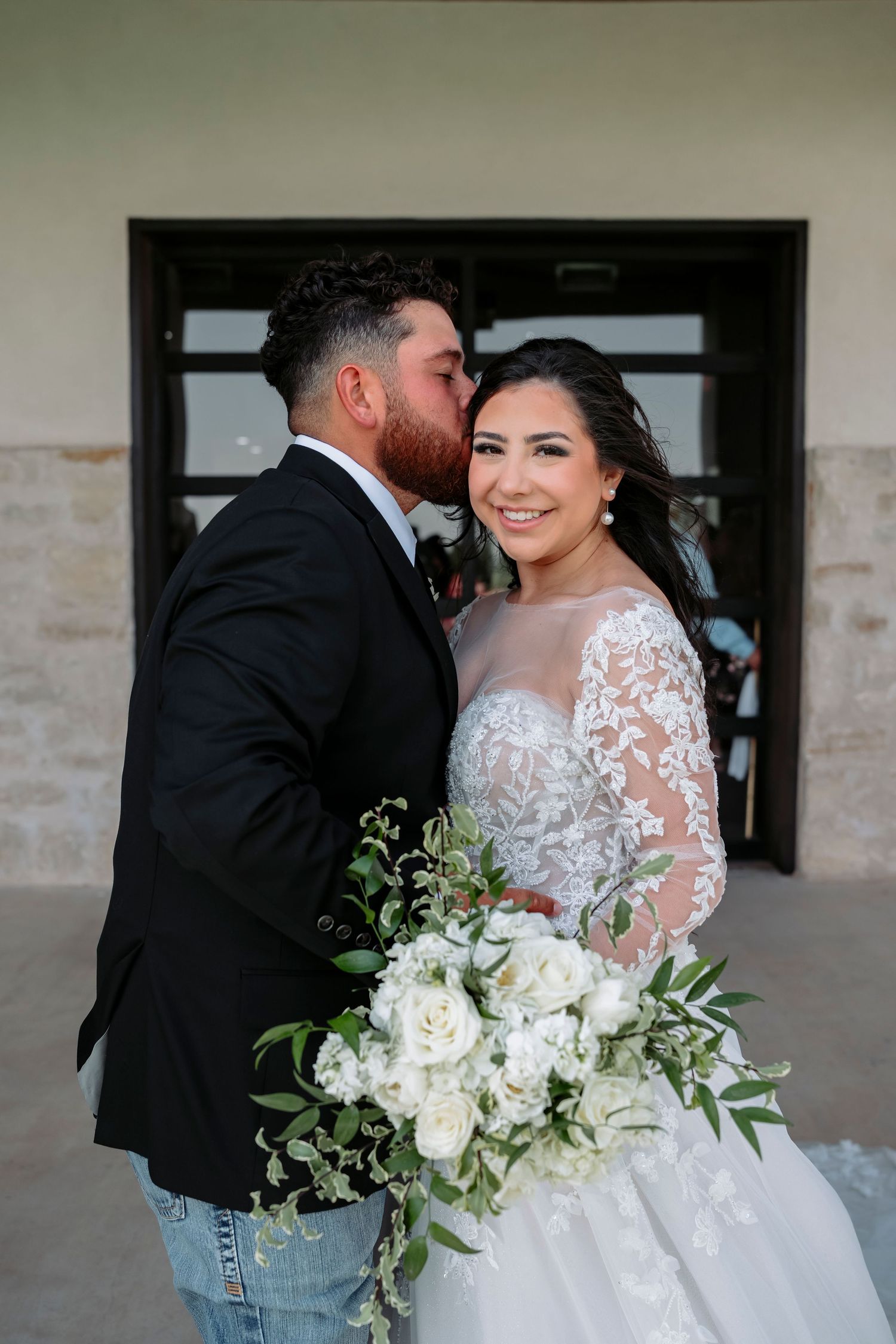 A romantic wedding photoshoot featuring a white lace gown and elegant bouquet of white flowers against a stone building.