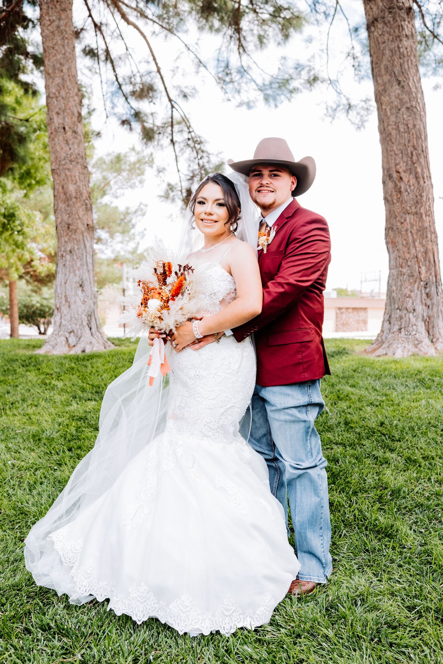 White wedding dress and western style attire photographed outdoors among pine trees.