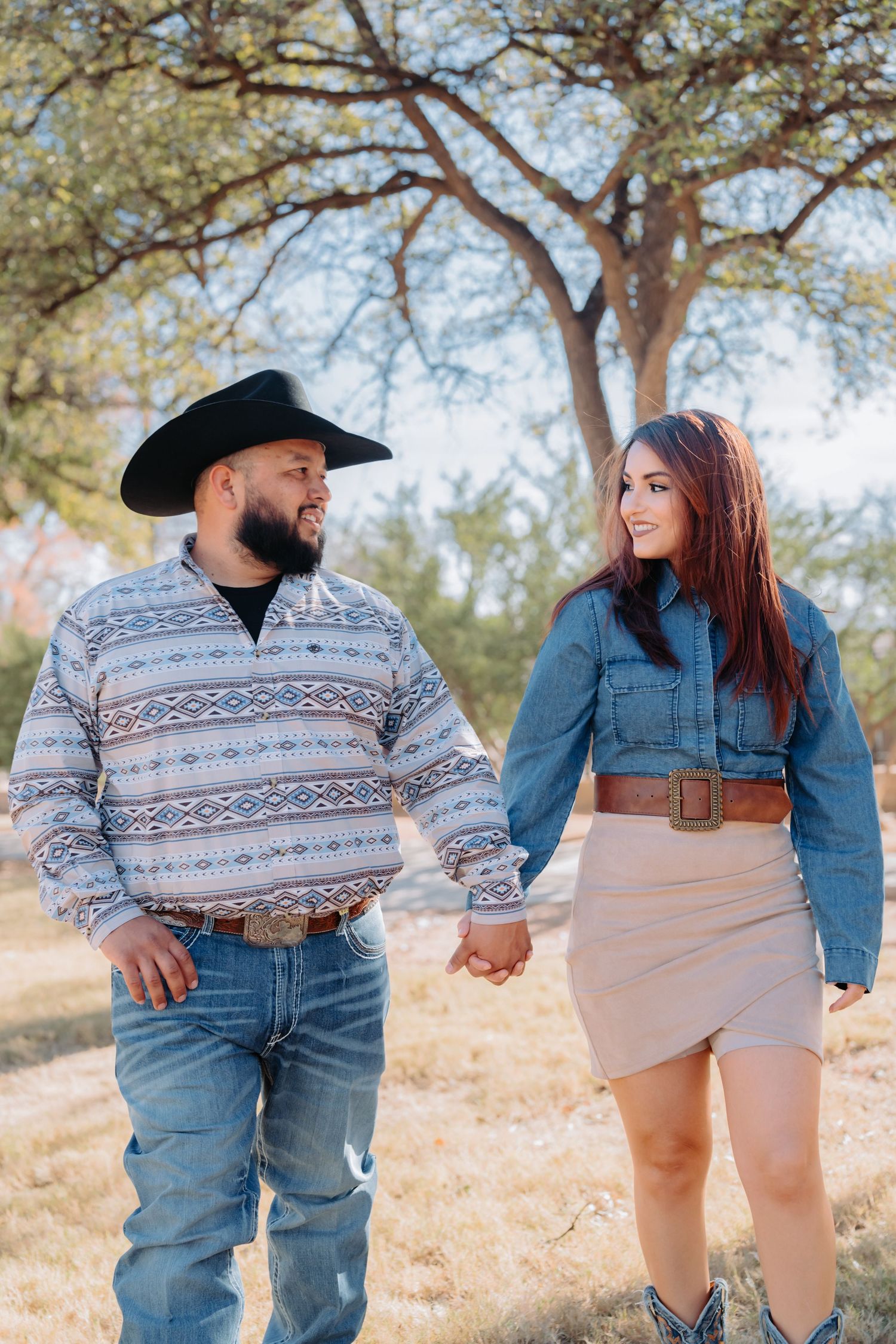 A romantic photoshoot featuring a couple in casual western attire on a sunny hillside.