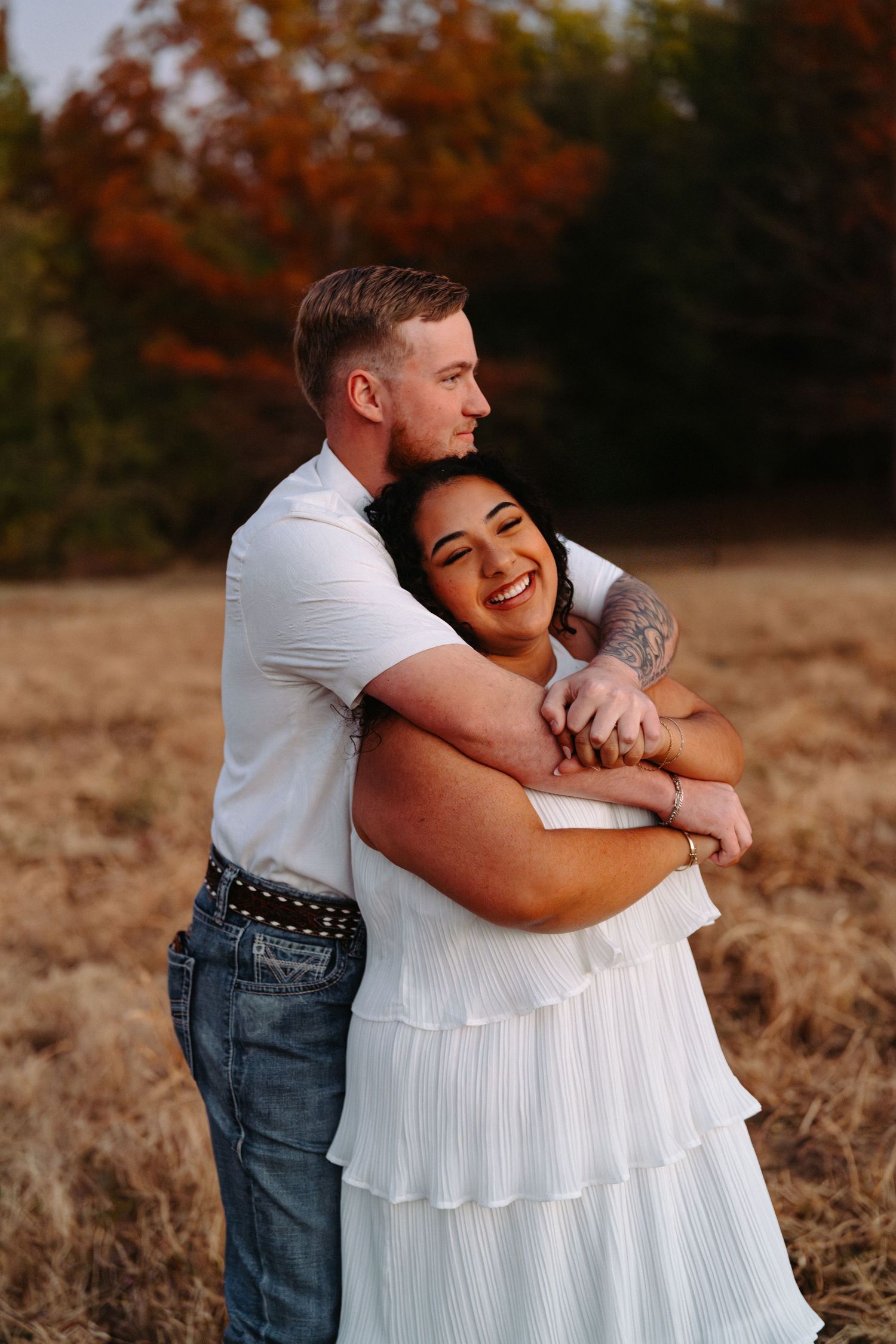Couple embracing and laughing together during autumn engagement photos in a field.