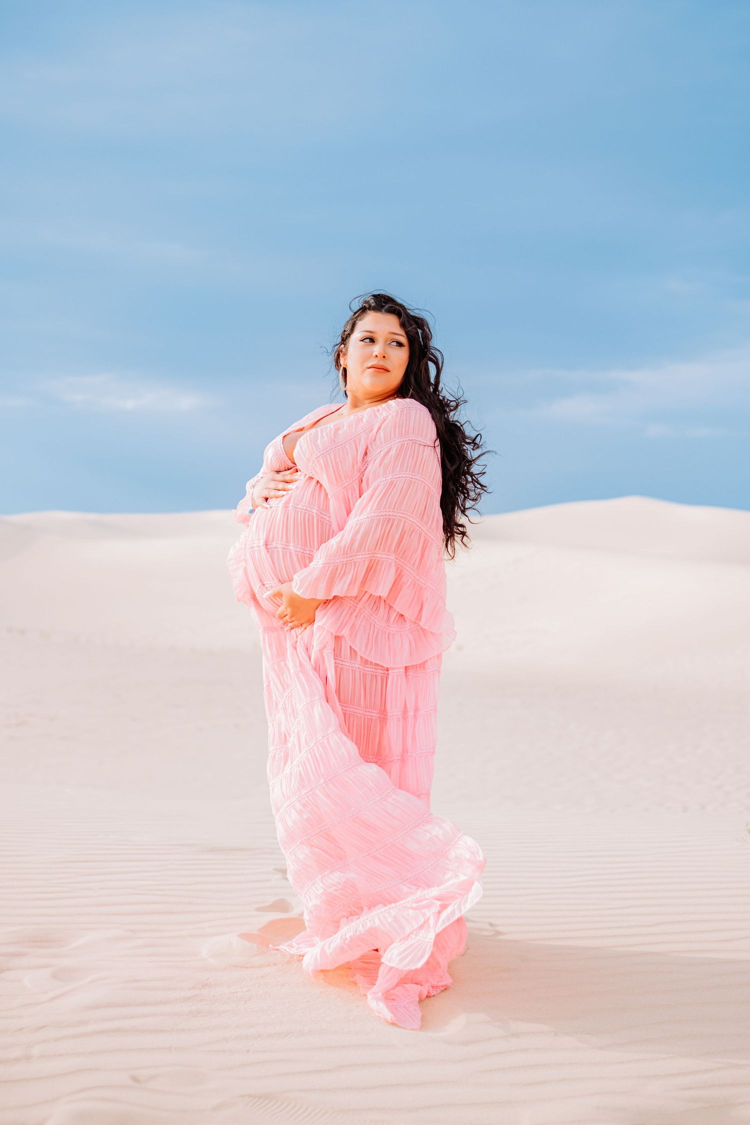 Person in billowing coral dress poses gracefully on white sand dunes.