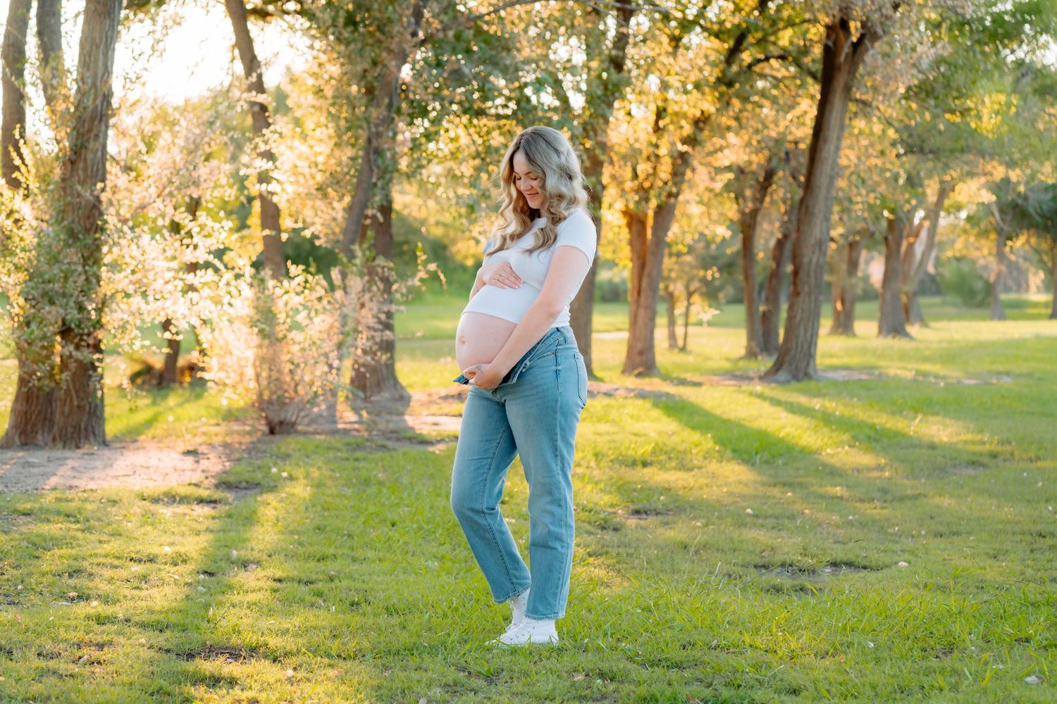 Artistic maternity photos taken in a park with warm sunset lighting.