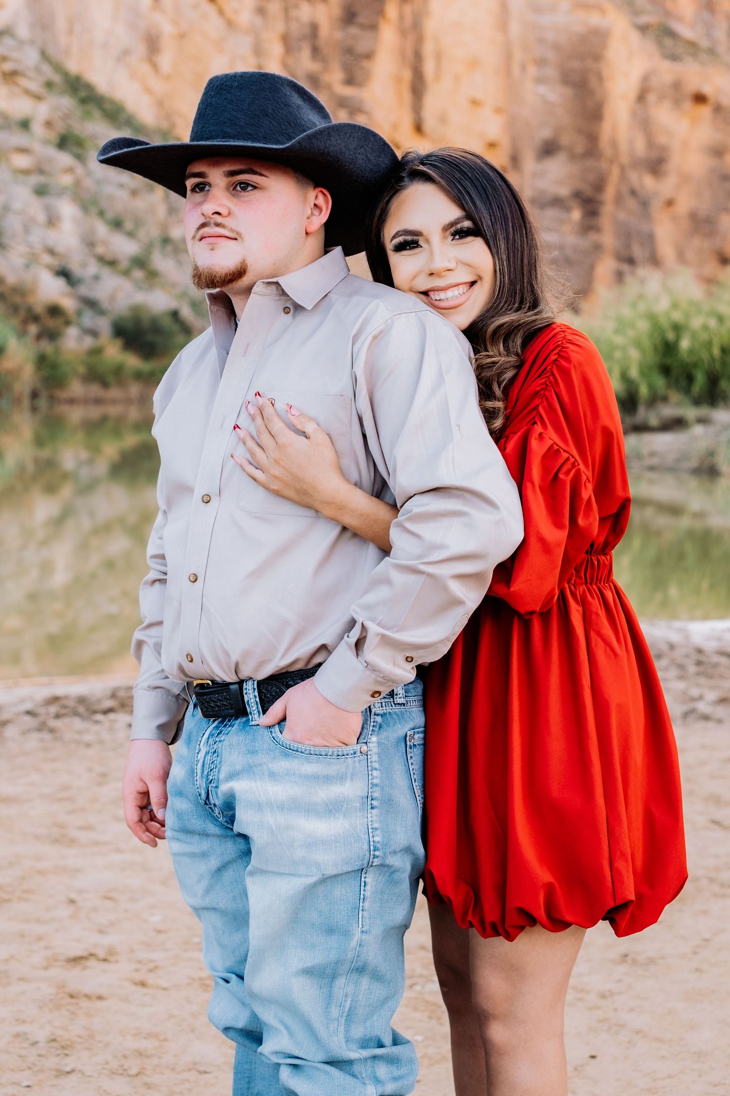 Couple in western-inspired outfits pose together against dramatic canyon landscape.