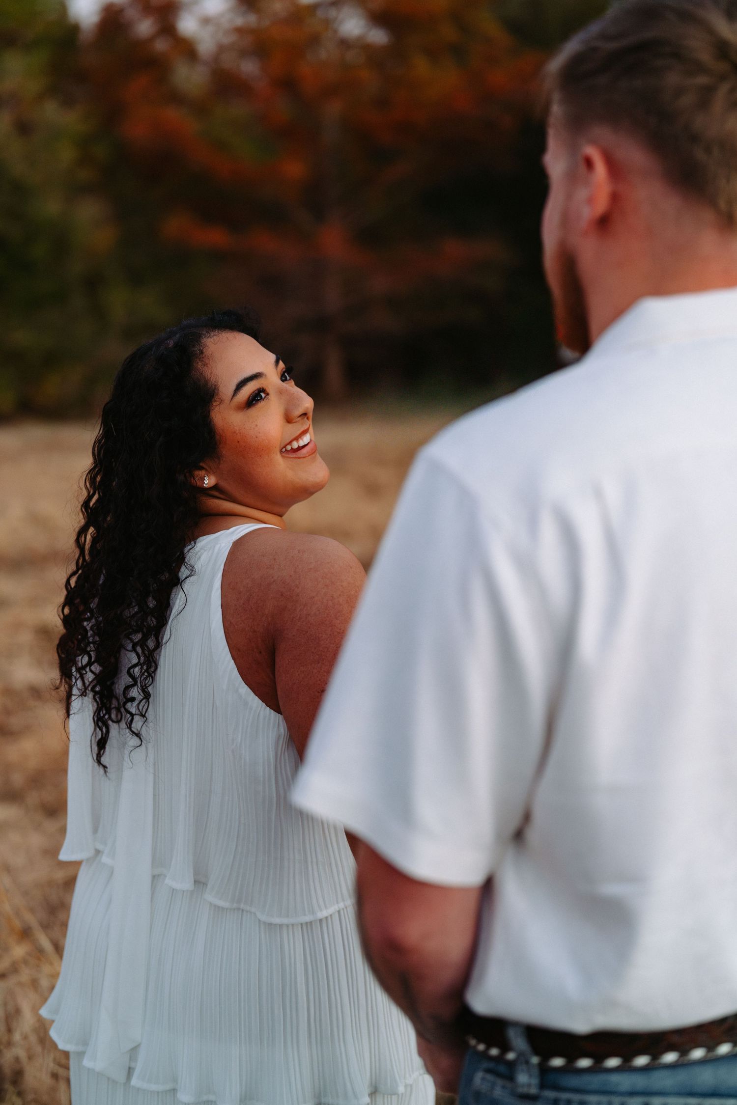 A couple shares intimate moments during an autumn photoshoot with fall foliage in the background.