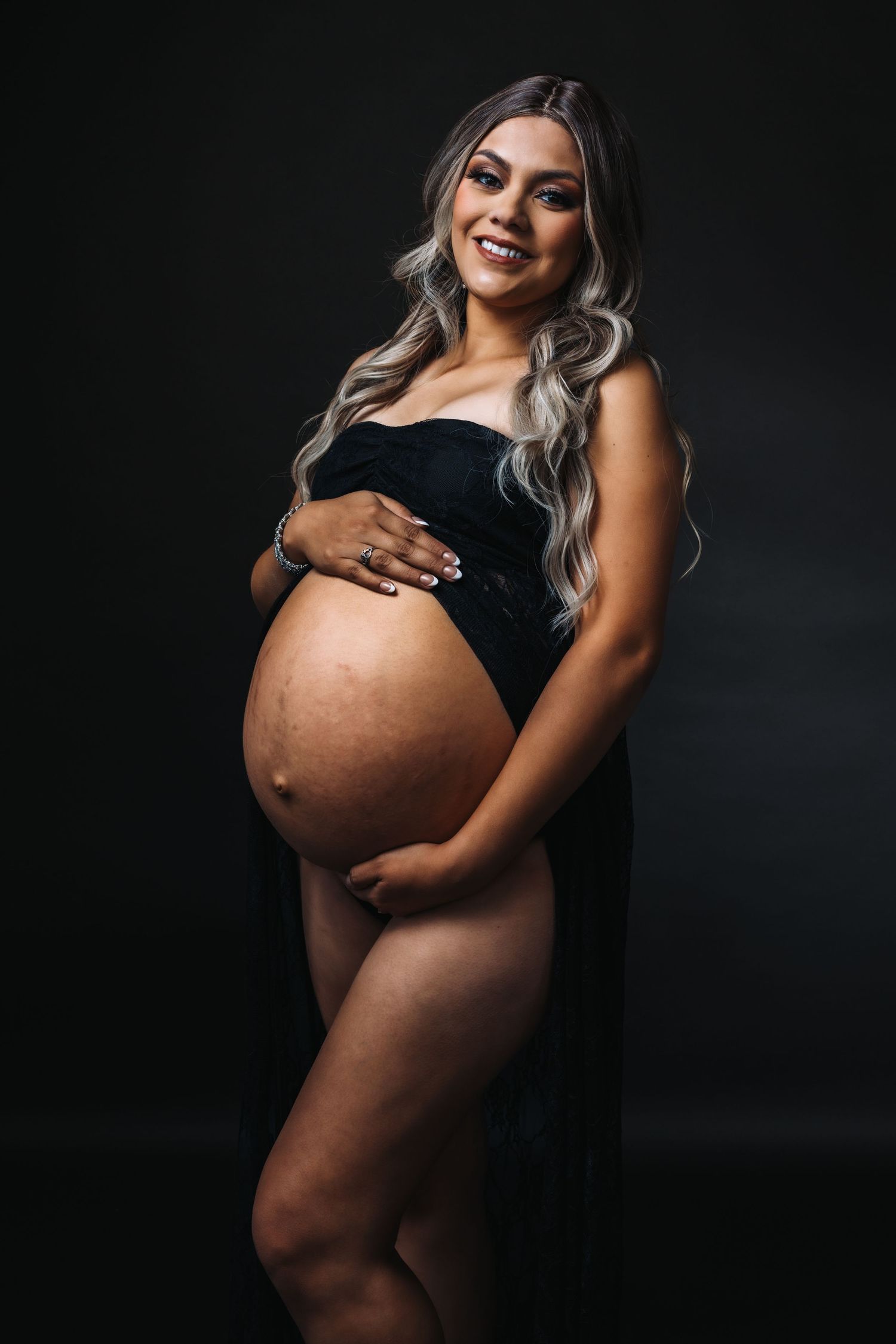 Artistic maternity photos featuring silhouette against dark background showing pregnant belly.