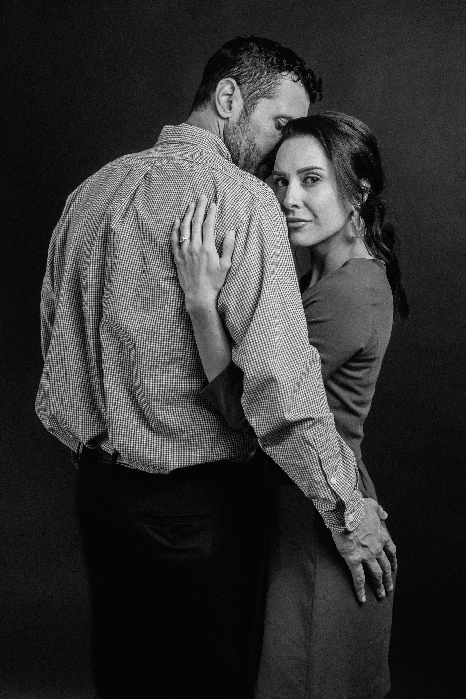 Black and white portrait of couple in intimate embrace against dark background.
