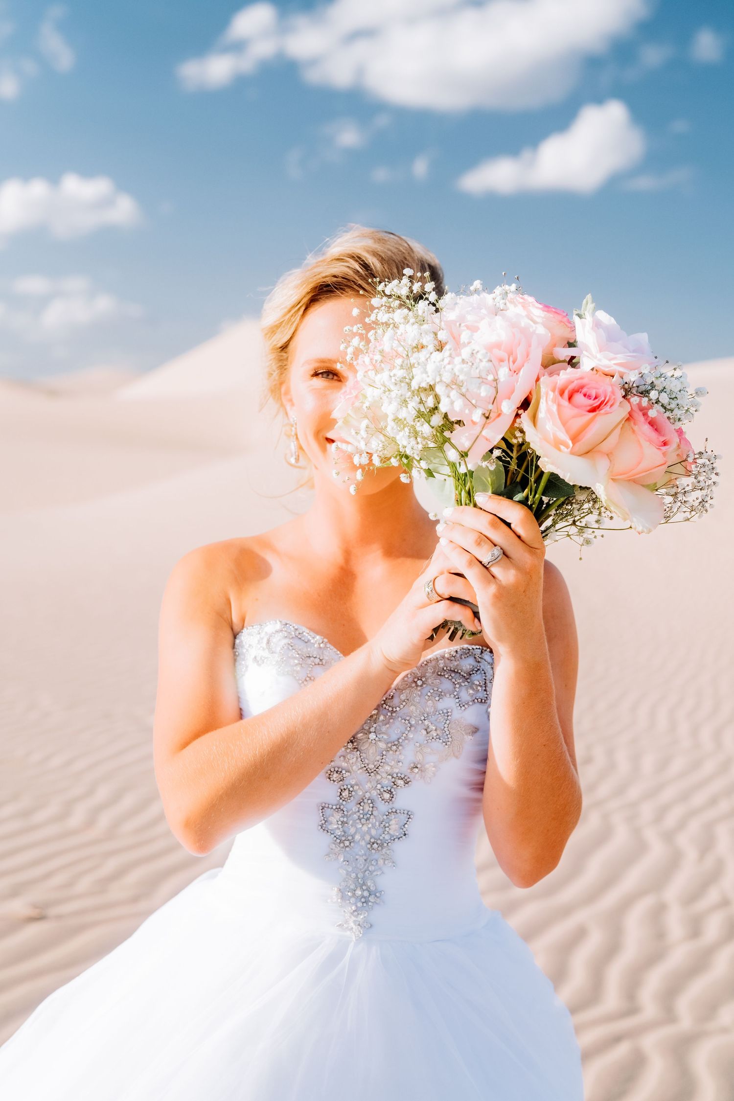 Bride holding pink roses and baby's breath bouquet against desert landscape.
