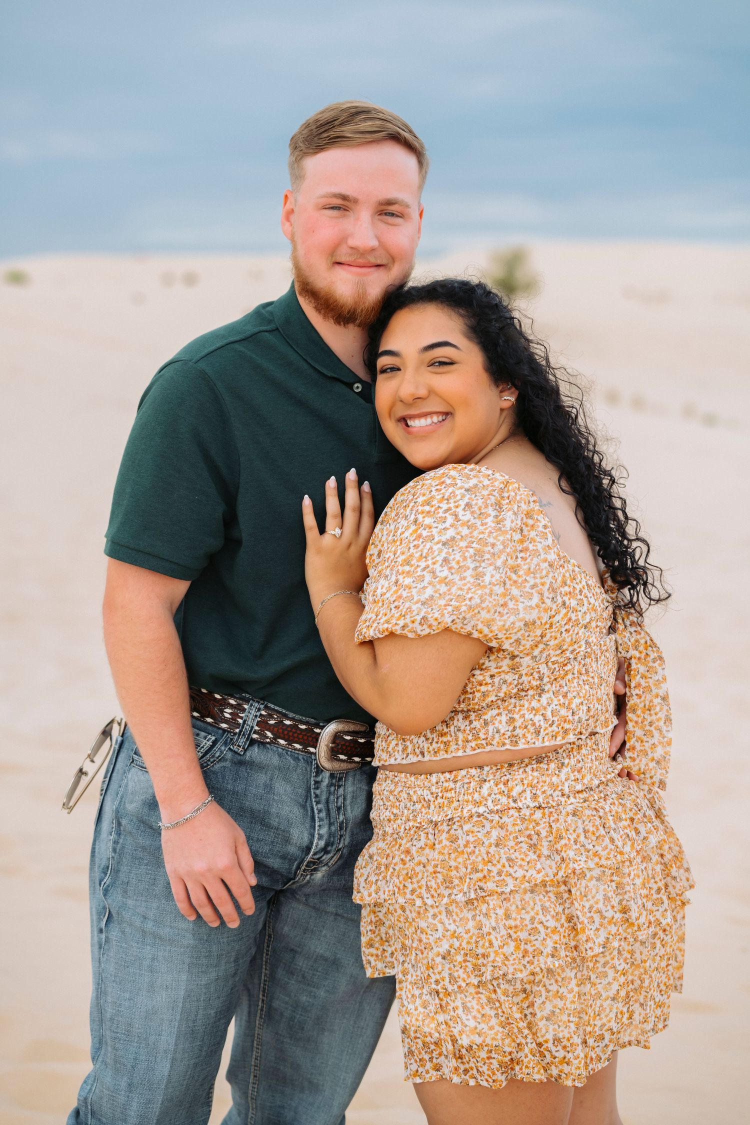 A couple embraces on a beach while showing off an engagement ring in a series of romantic photos.