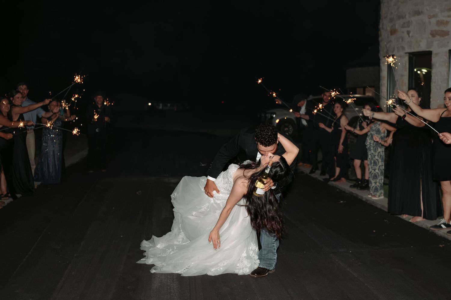 Wedding couple performs a romantic dip dance move on a dark dance floor surrounded by guests.