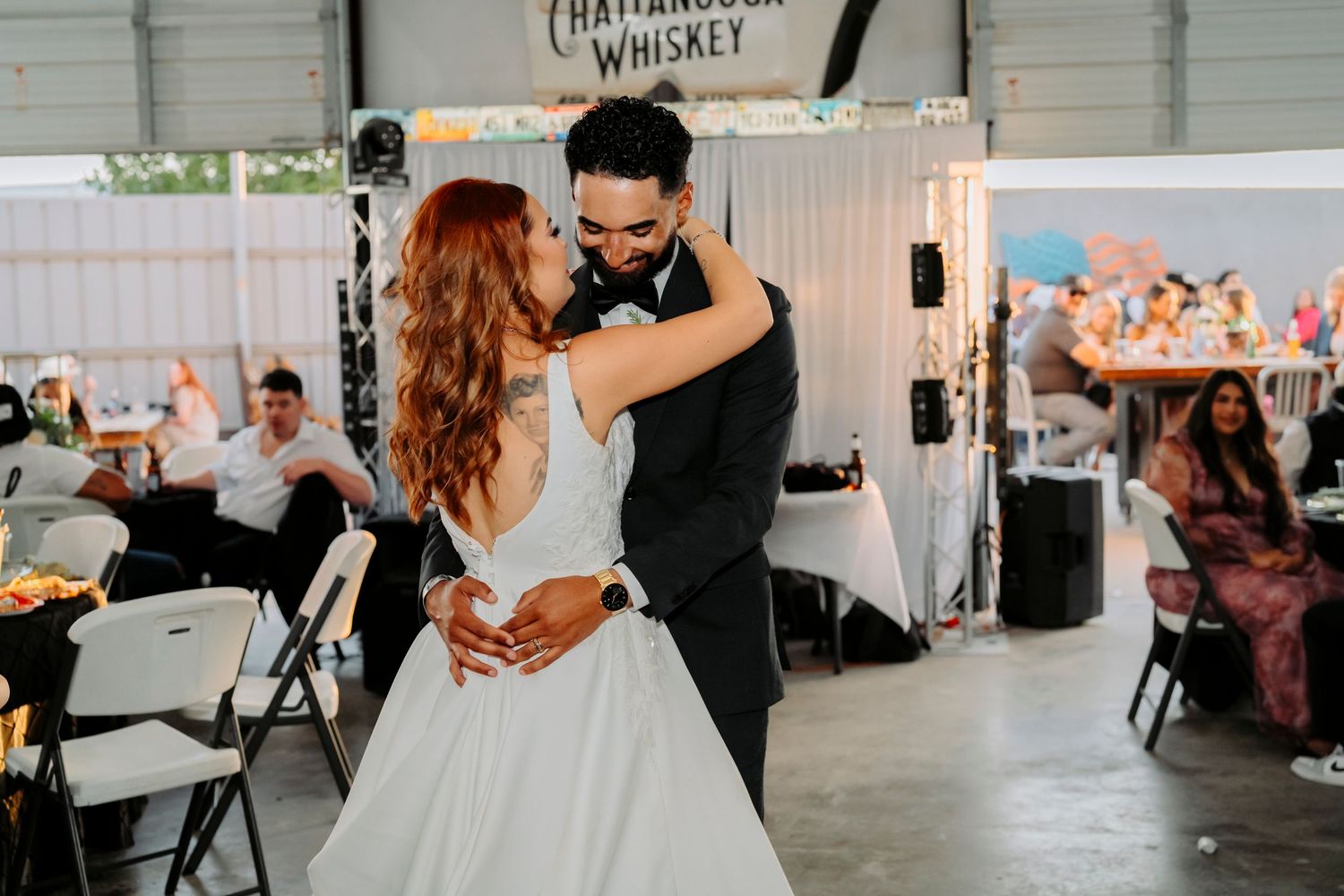 A couple sharing their first dance at a rustic wedding reception under a Chattanooga Whiskey sign.