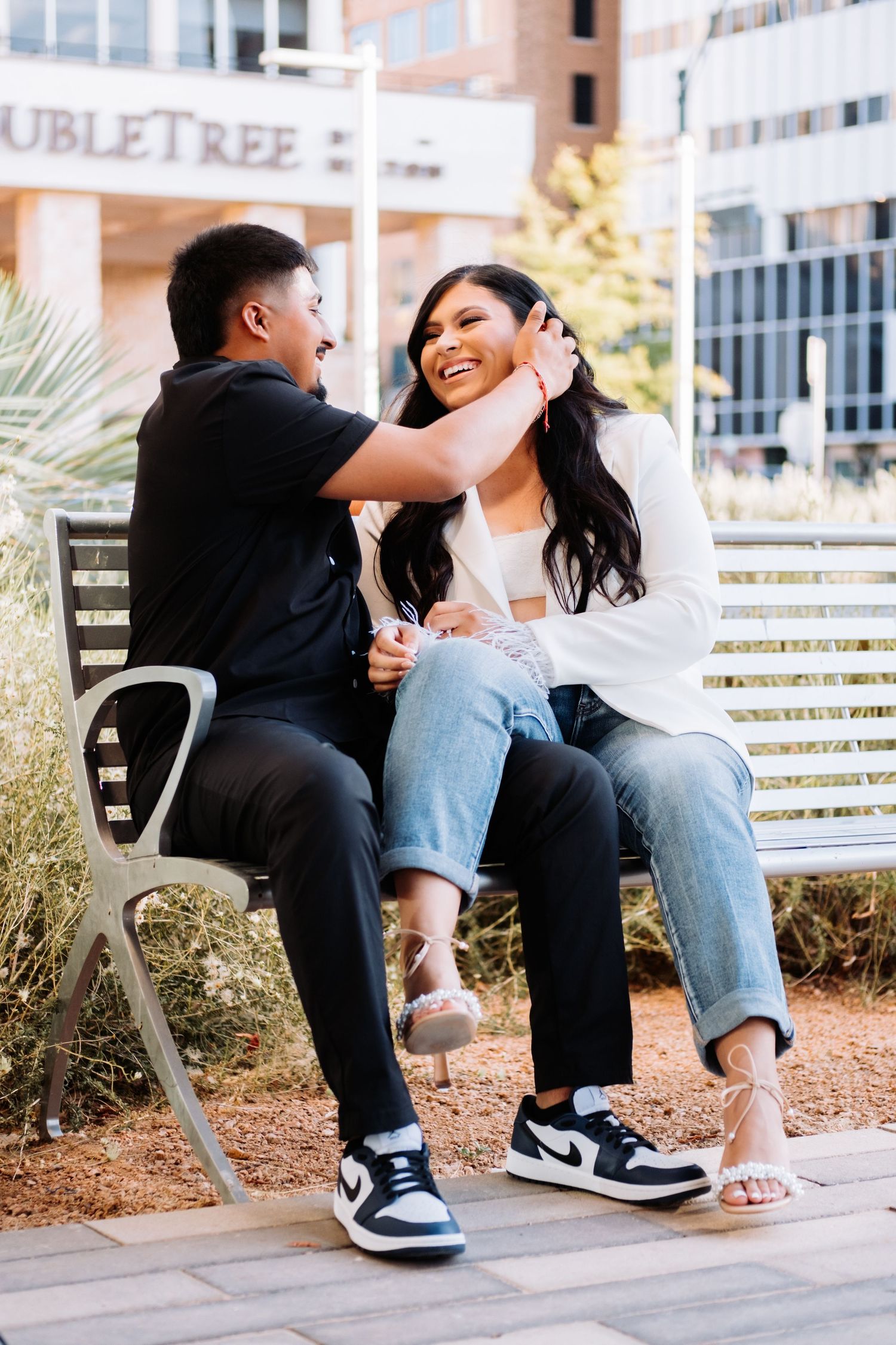 A couple shares laughter while sitting on outdoor furniture near a modern building.