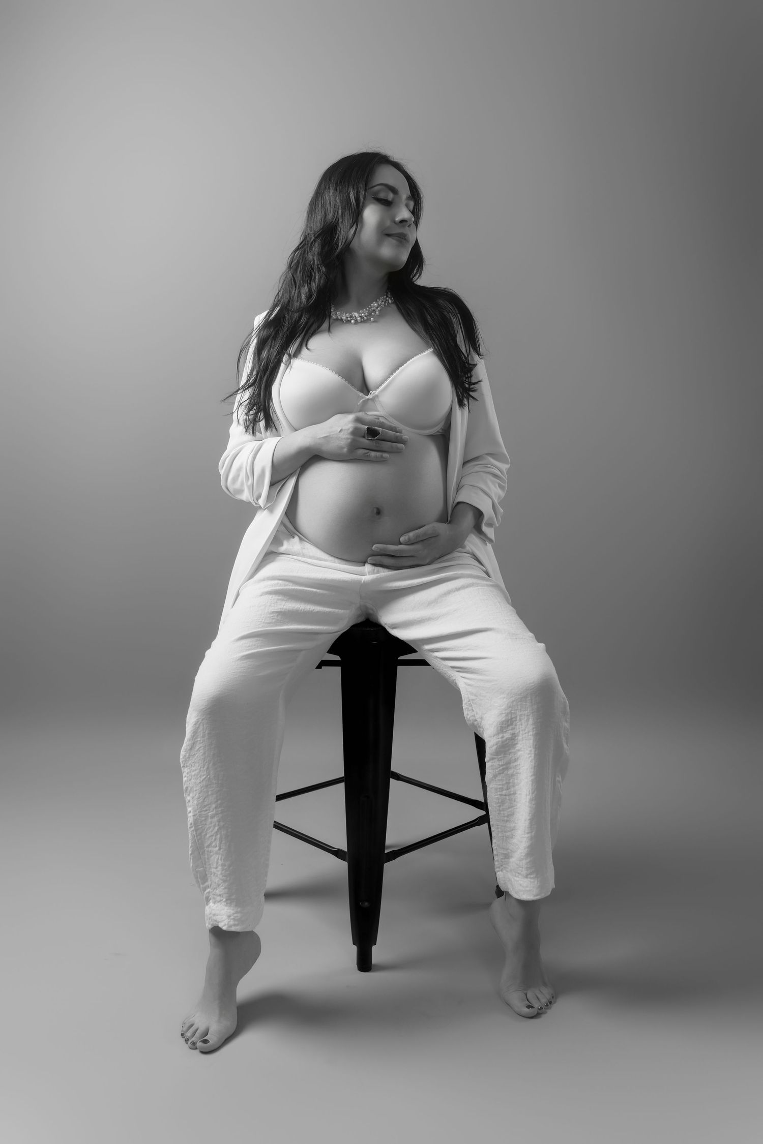 Dramatic black and white maternity portraits showcasing natural poses on a studio stool.