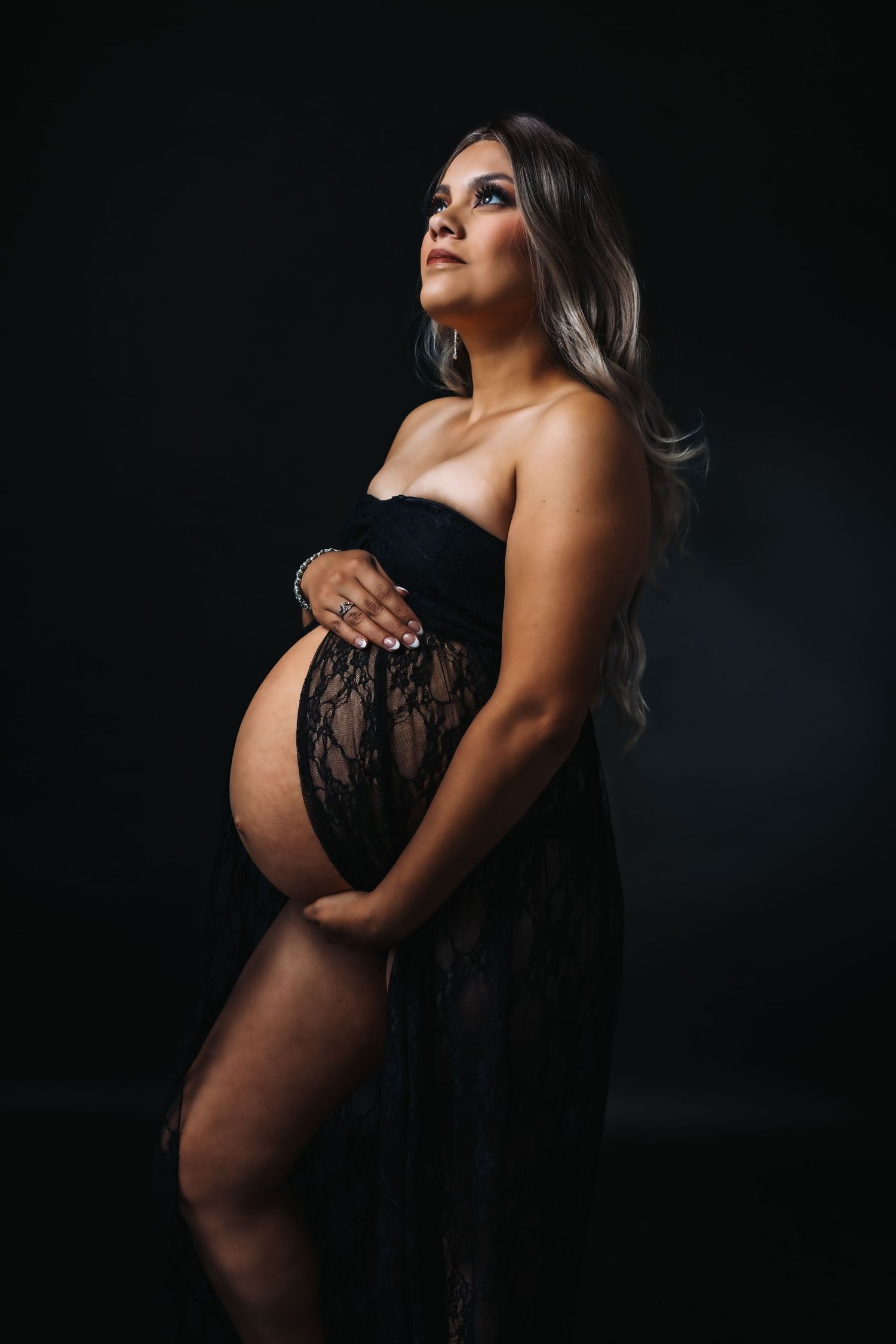Elegant silhouette maternity portraits featuring black lace against dramatic dark backdrop.