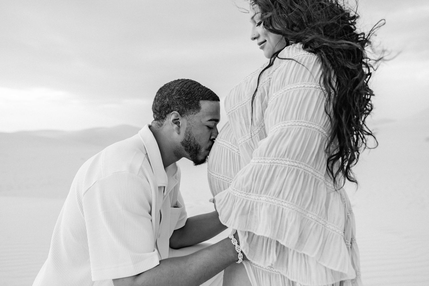Romantic black and white photos of couple embracing on sand dunes.