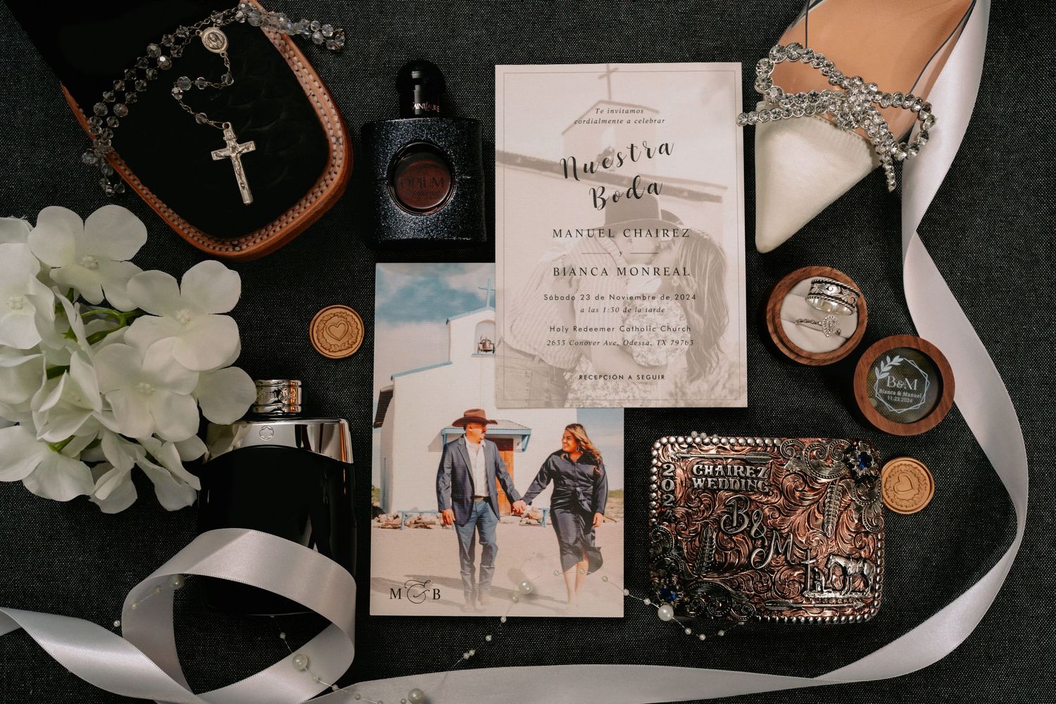 Wedding details flatlay with invitation, rings, jewelry, and decorative elements on dark background.