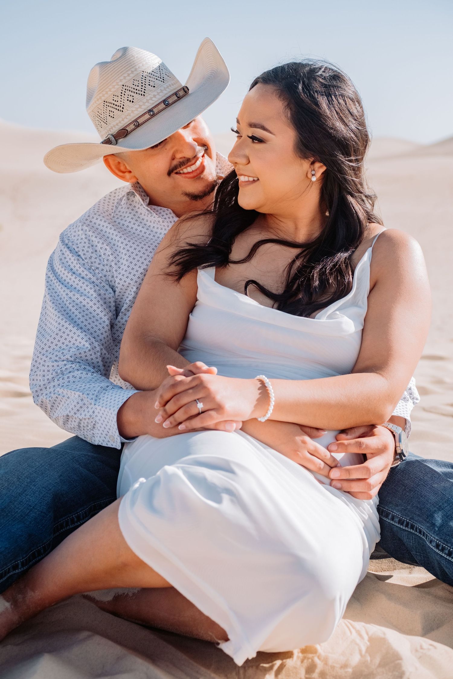 Couple embraces while taking romantic photos in desert sand dunes.