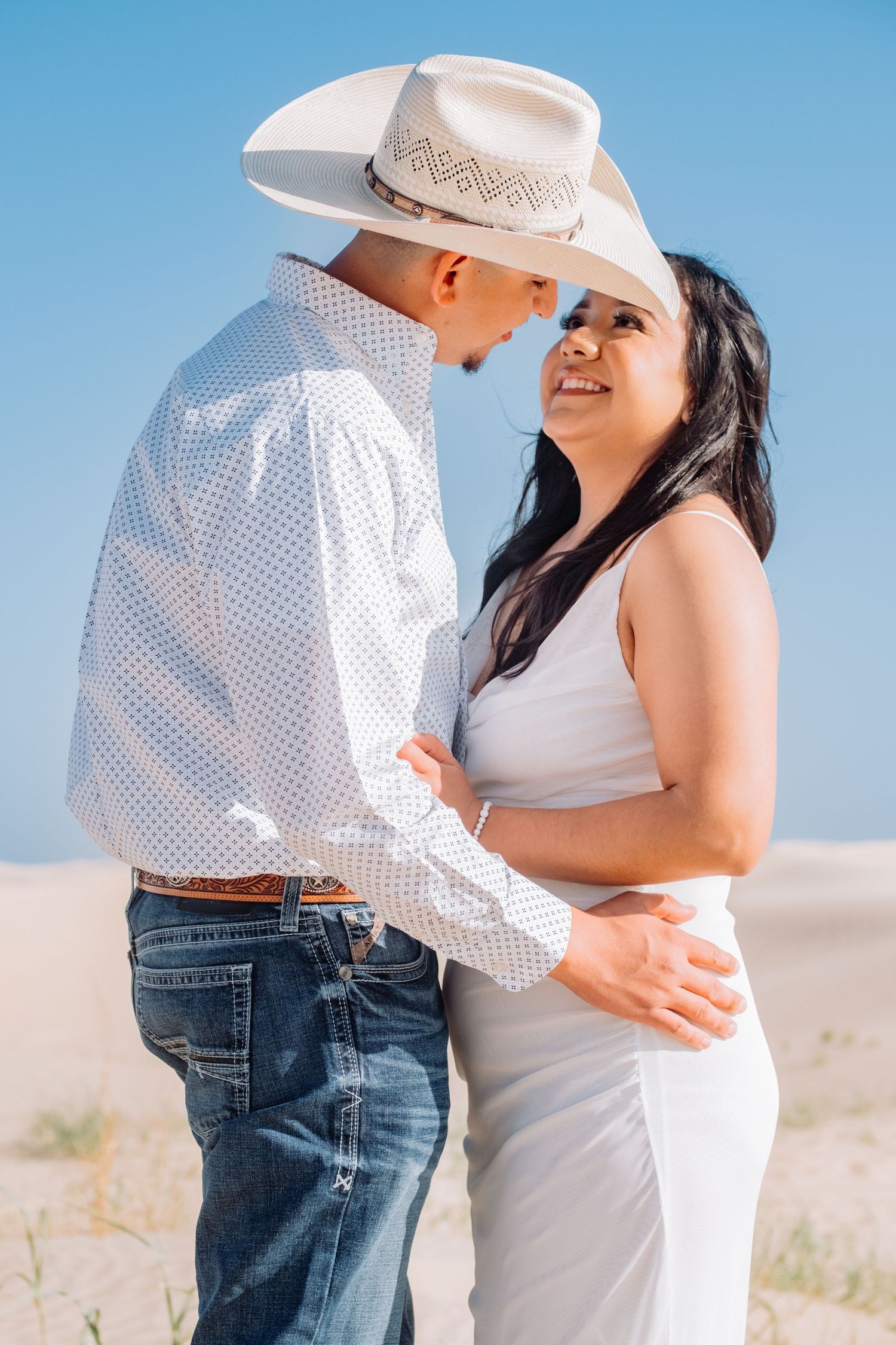 Happy couple in cowboy attire laughing together on sand dunes.