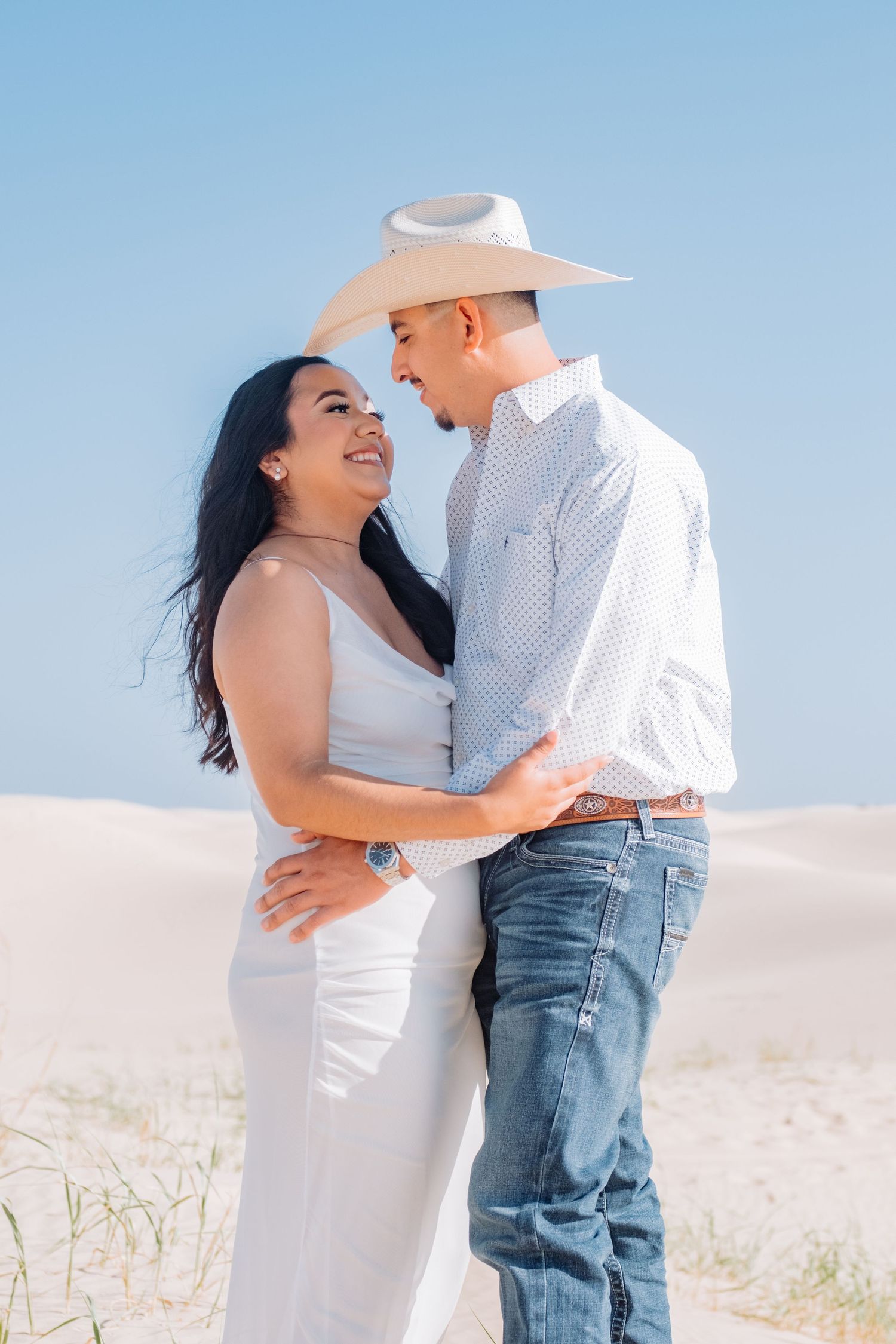 Couple in white and denim share romantic moment on sandy terrain.