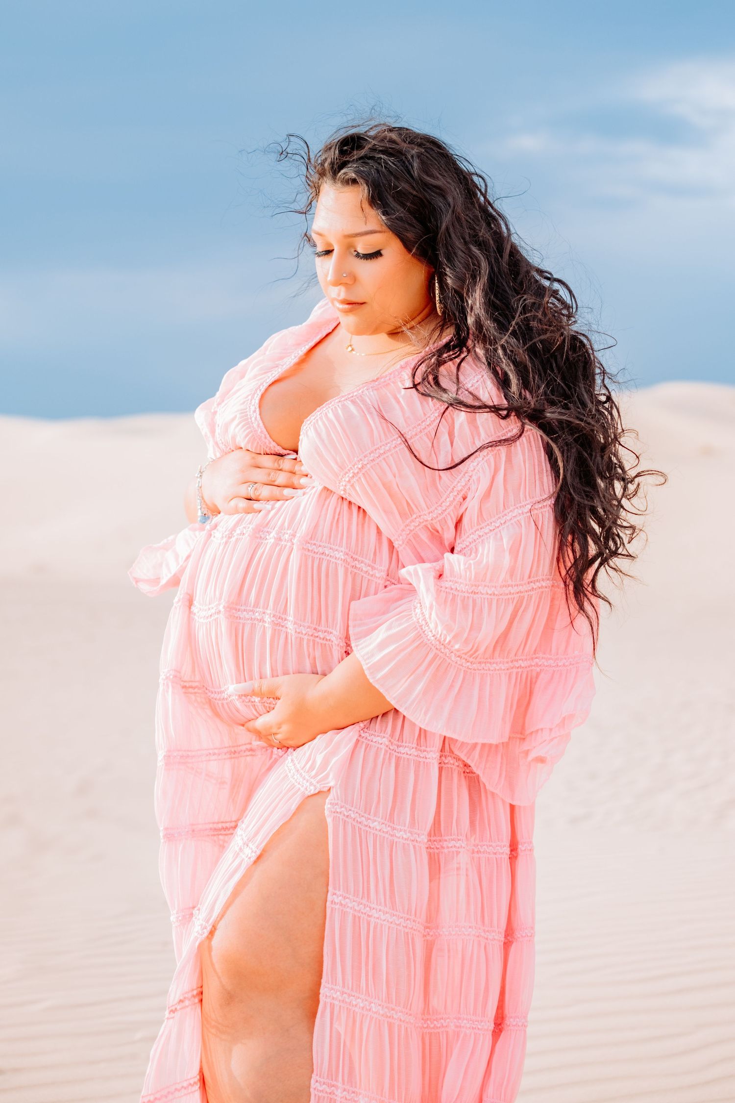 Woman in ruffled coral dress poses against sand dunes and blue sky.