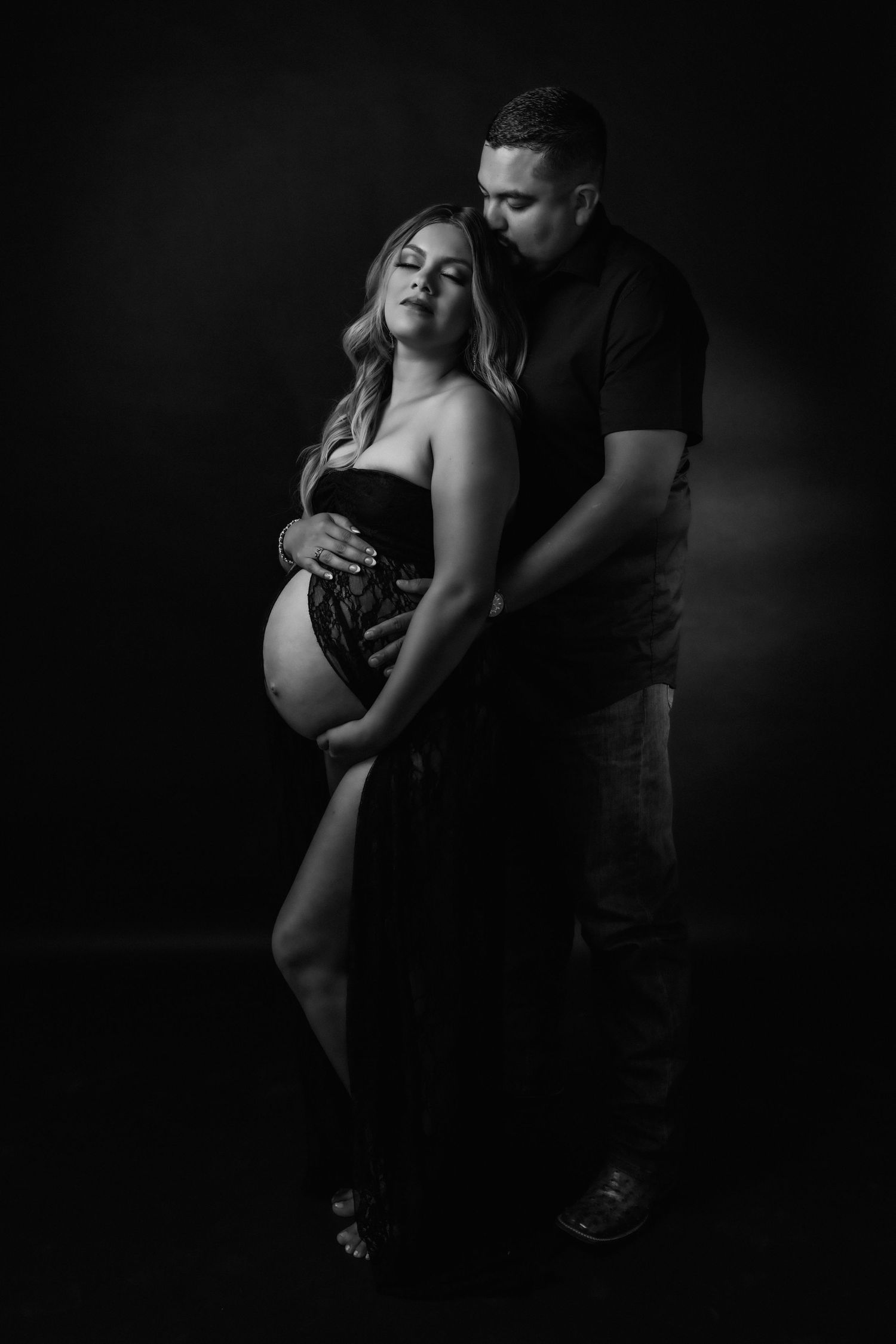 Intimate couple's maternity portrait in dark studio setting with emotional connection.
