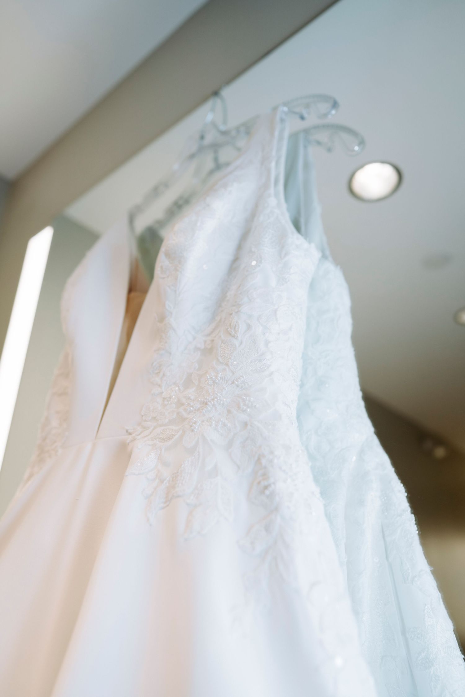 Close-up detail of white lace wedding dress bodice hanging against light background.