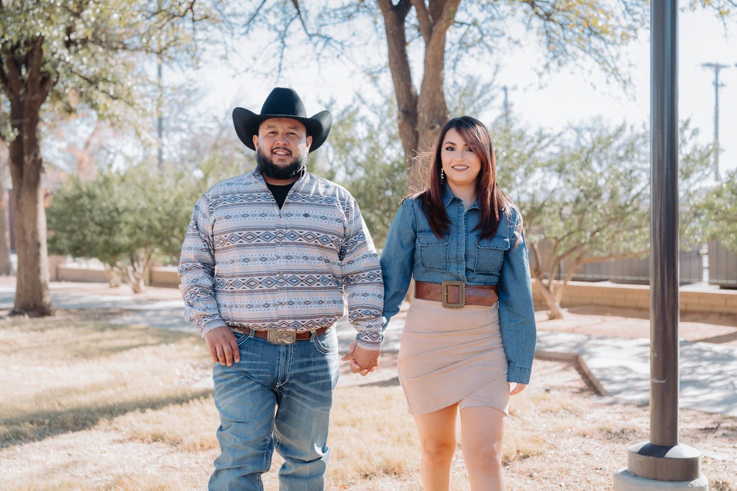 Happy couple in western attire poses playfully during outdoor photoshoot.