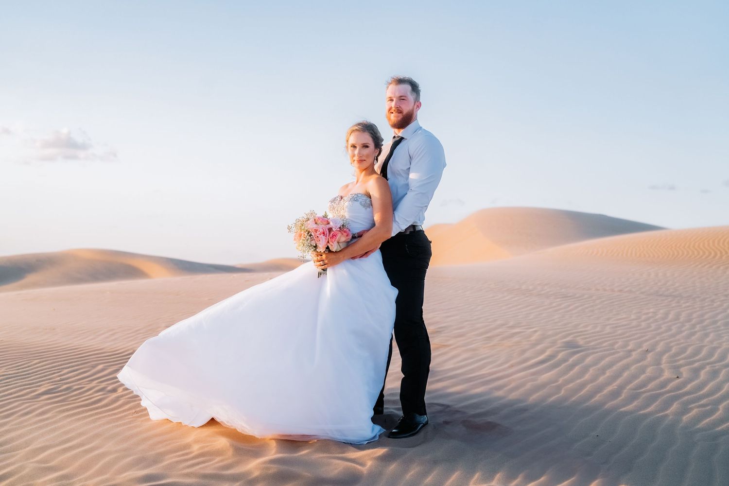 Wedding couple posing artistically on sandy dunes during a desert photo session.