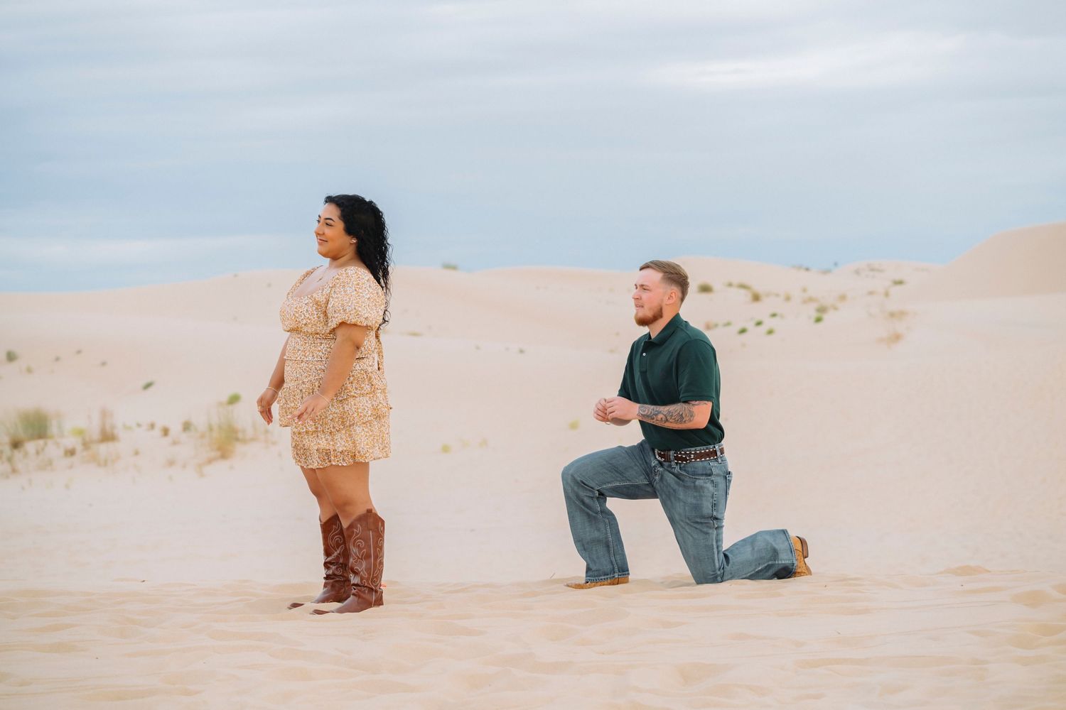 Couple in soft earth tones embracing on sandy dunes during golden hour photo session.