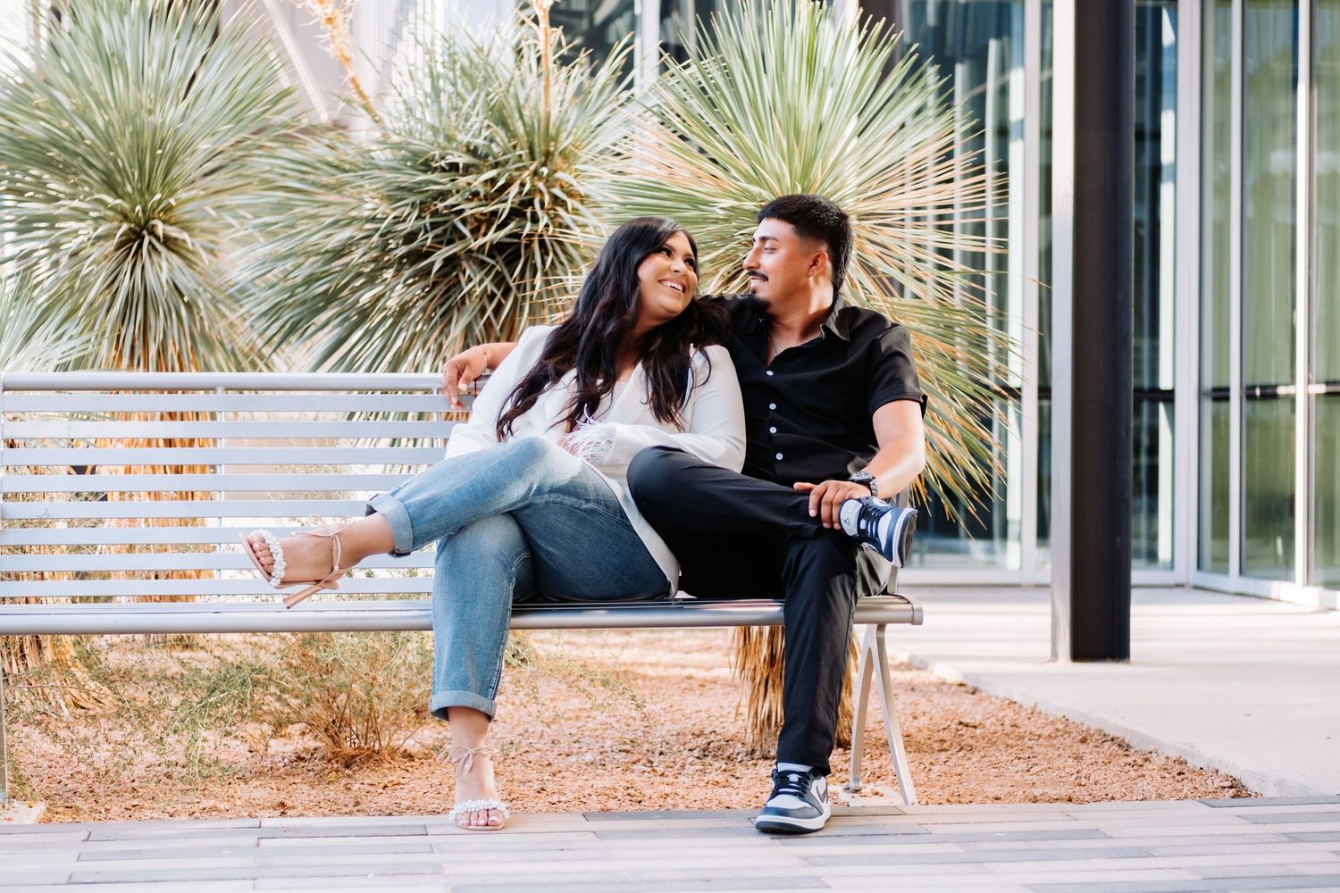 A couple sharing moments on an outdoor bench with desert plants in the background.