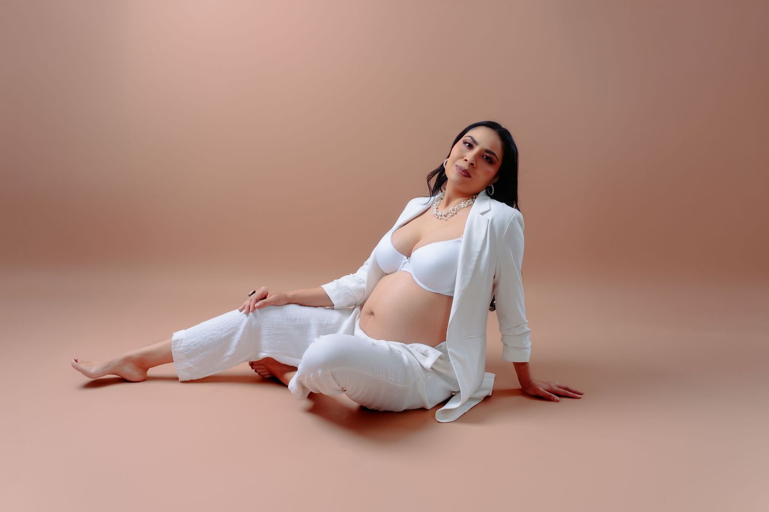 Ethereal maternity photos on a rose-colored backdrop with flowing white clothing.