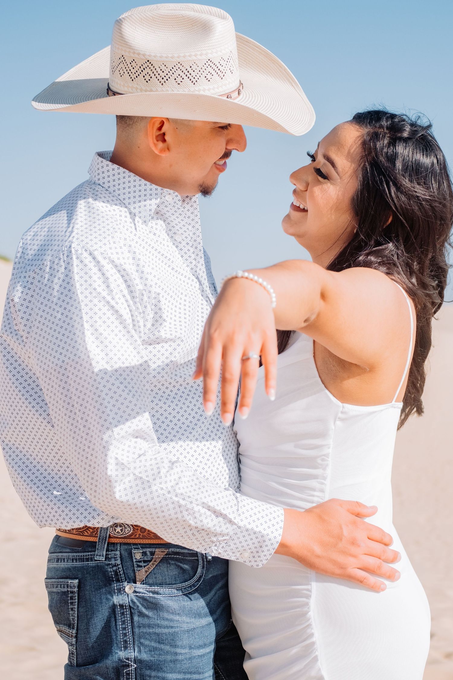 Couple in western wear sharing intimate moment against blue sky.