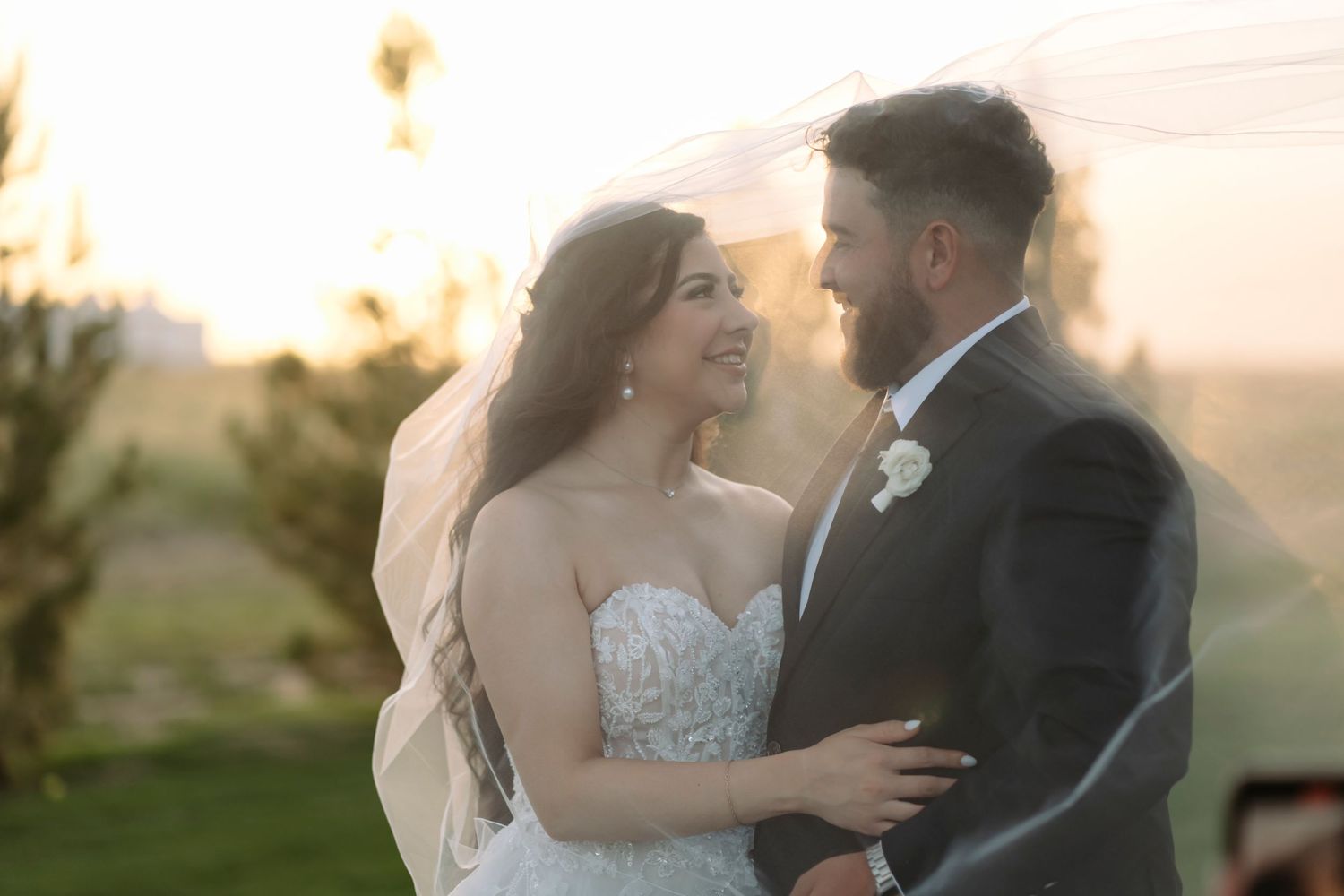 A couple in wedding attire embraces during golden hour in a romantic outdoor setting.