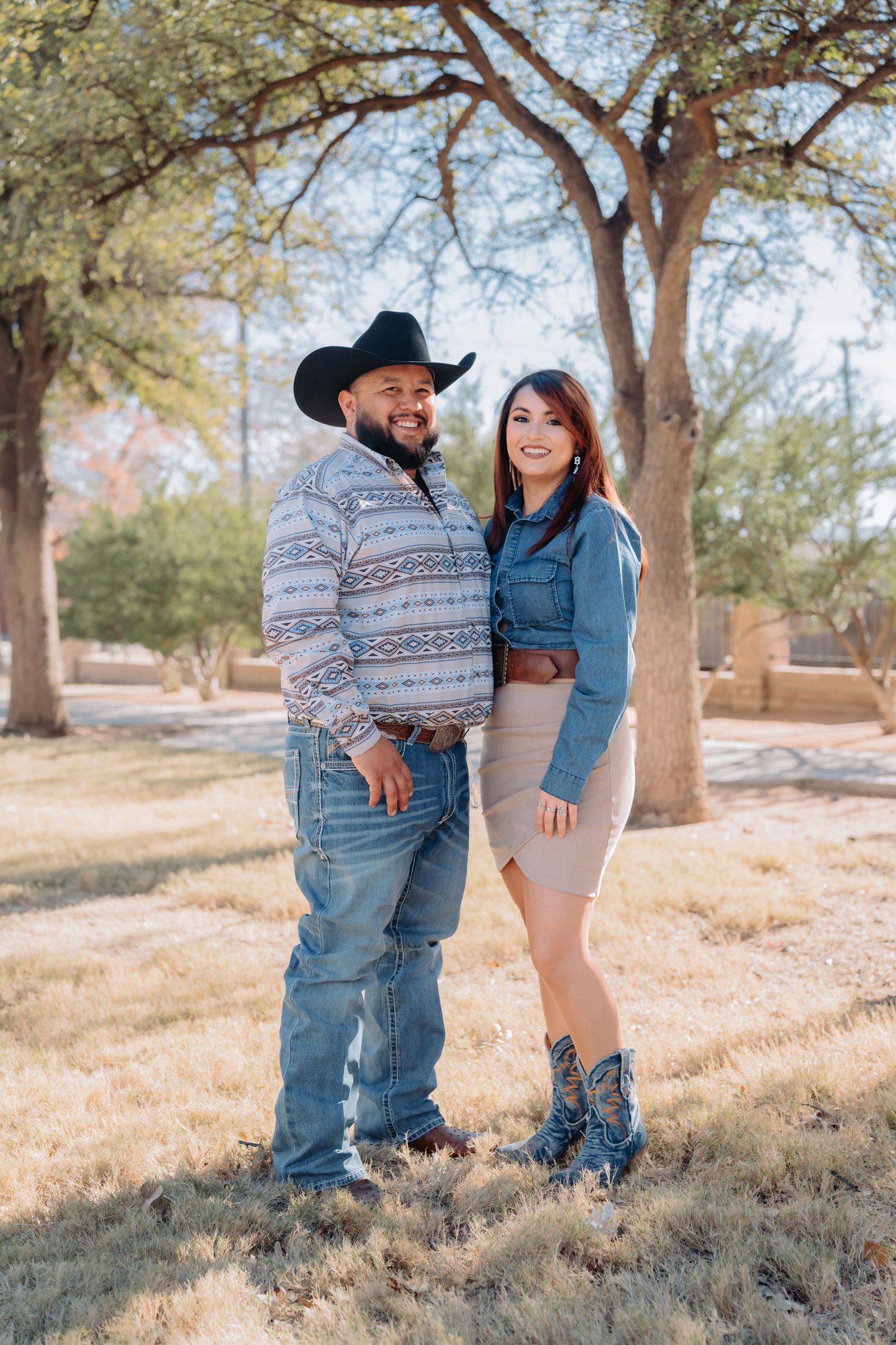 A couple poses playfully on a grassy hill during an autumn outdoor photoshoot.