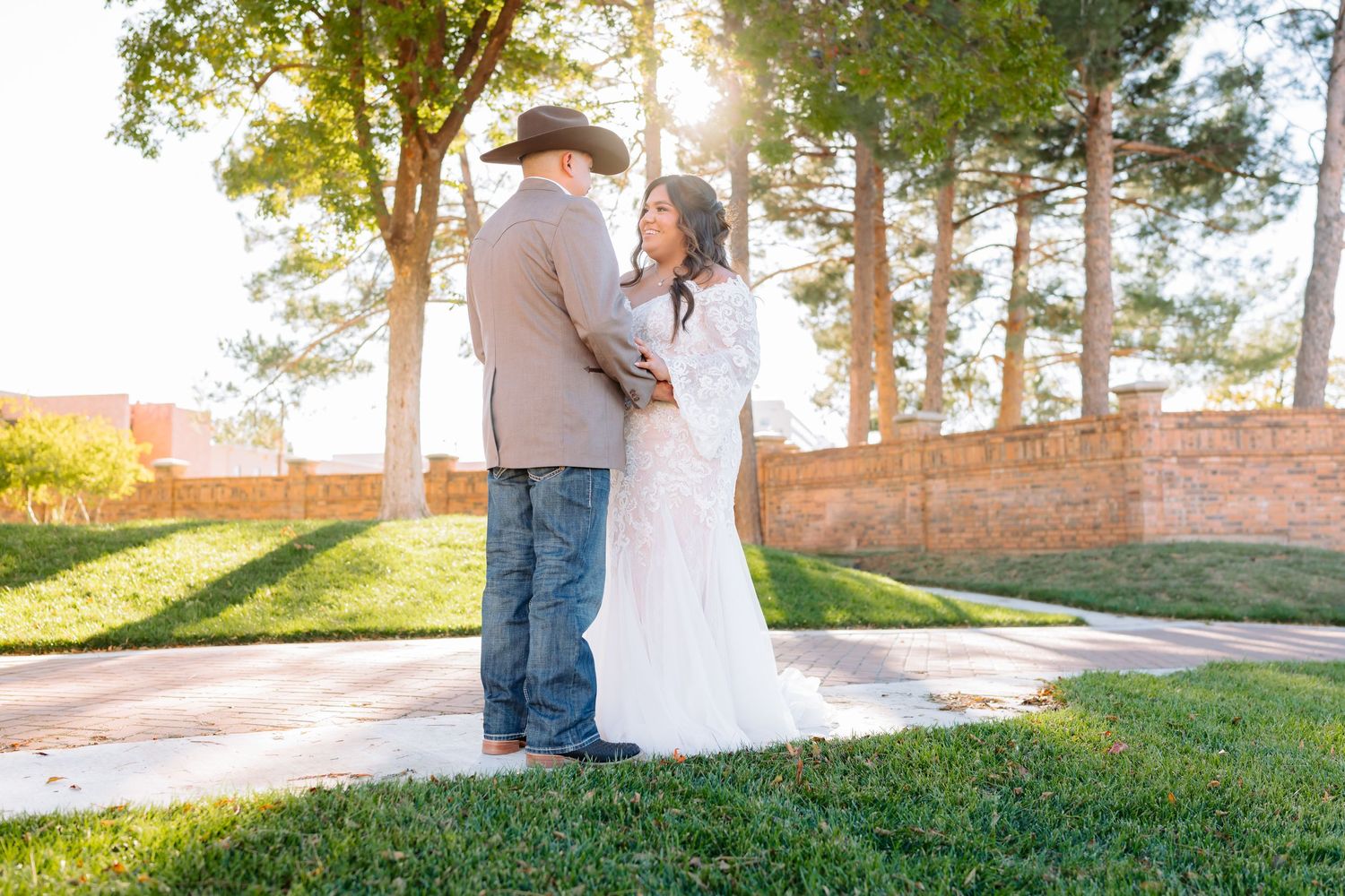 Sun-drenched wedding photos taken on a grassy hill with tall trees in the background.