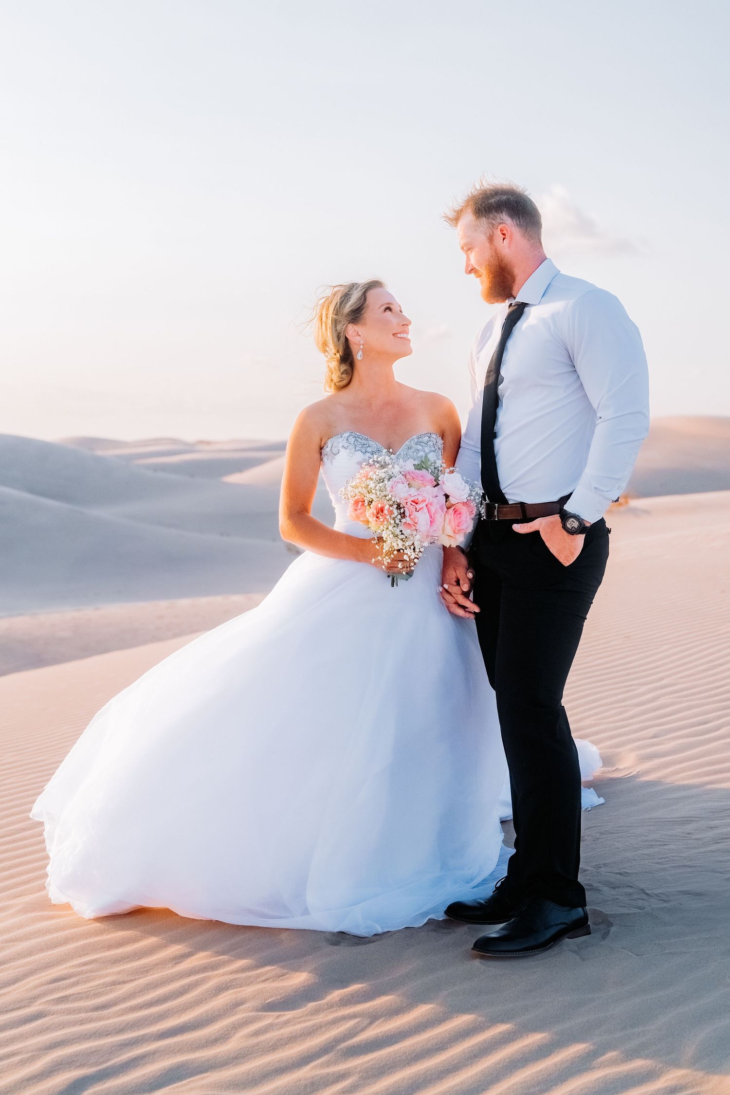 Romantic desert wedding portraits with couple posing against sweeping sand dunes.