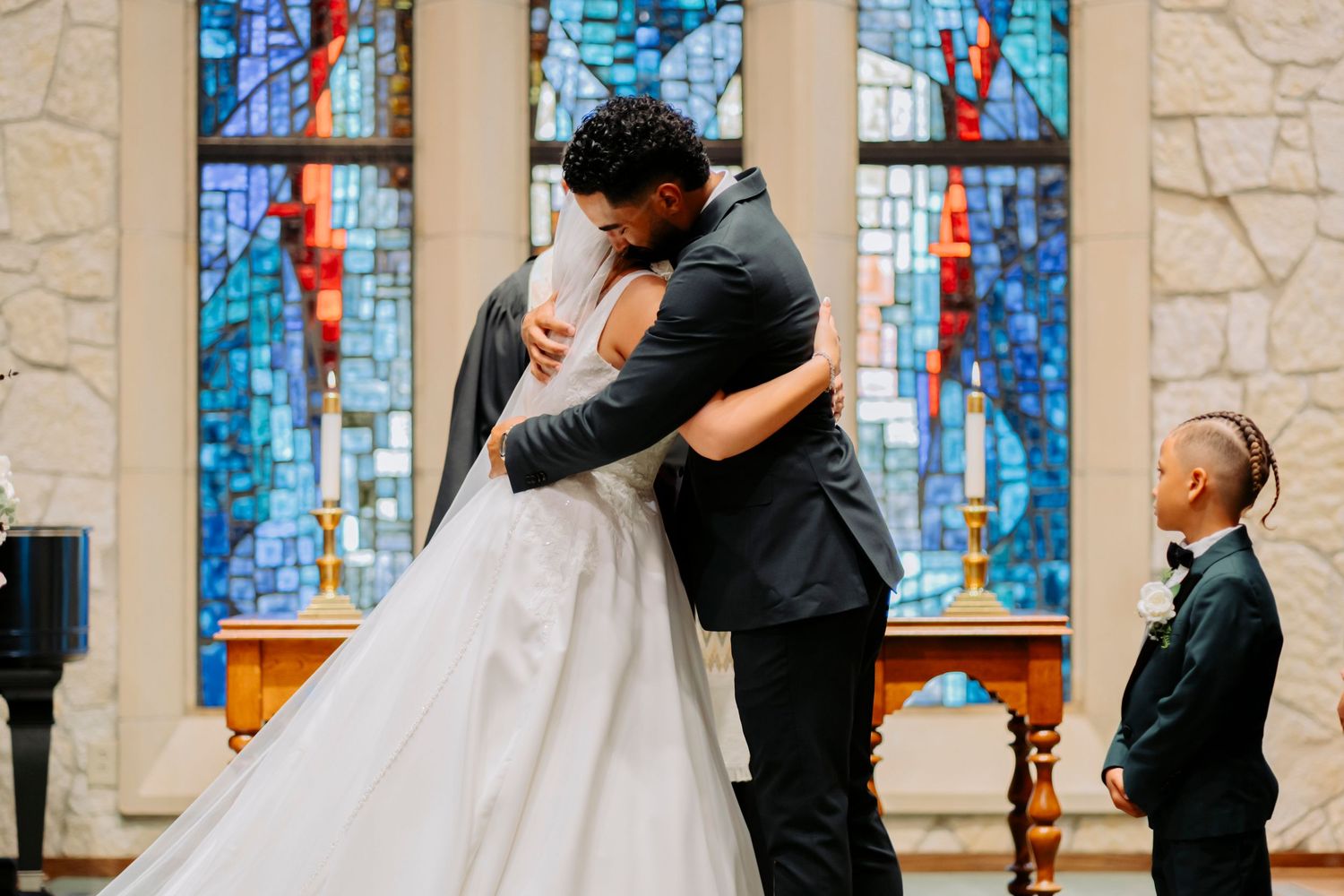 Romantic moment during wedding ceremony with blue stained glass windows in background.