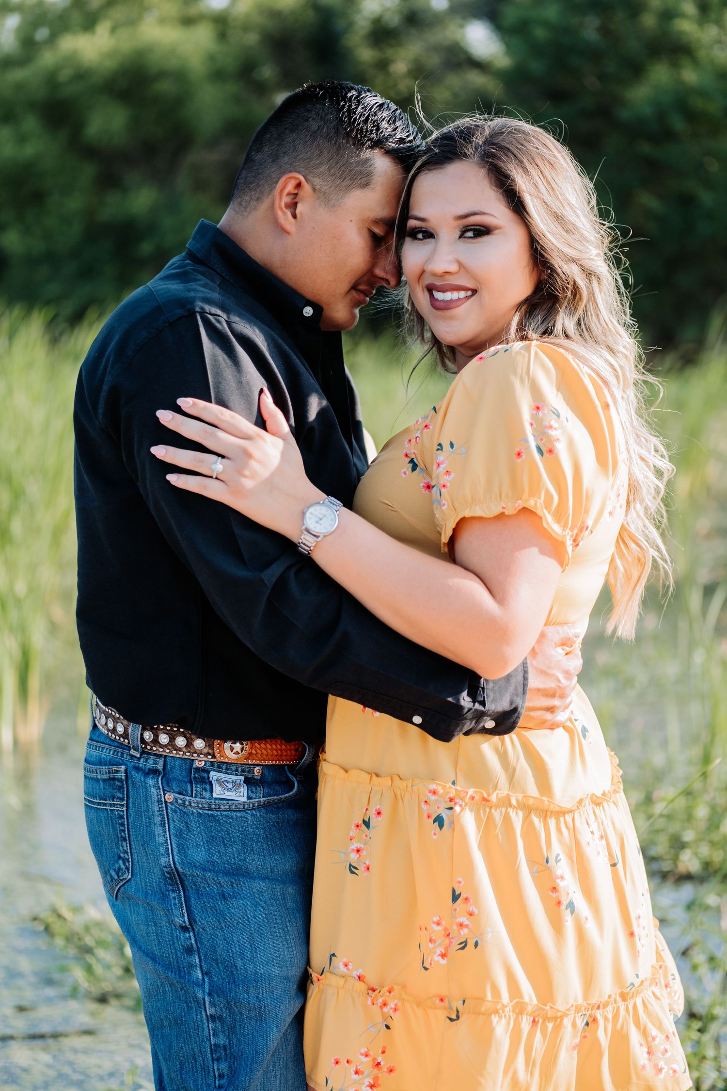 Couple embraces outdoors, with woman in yellow floral dress and man in black shirt.