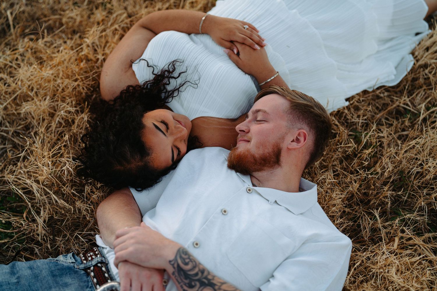 Couple sharing intimate moments while lying in golden grass during a rustic outdoor photoshoot.