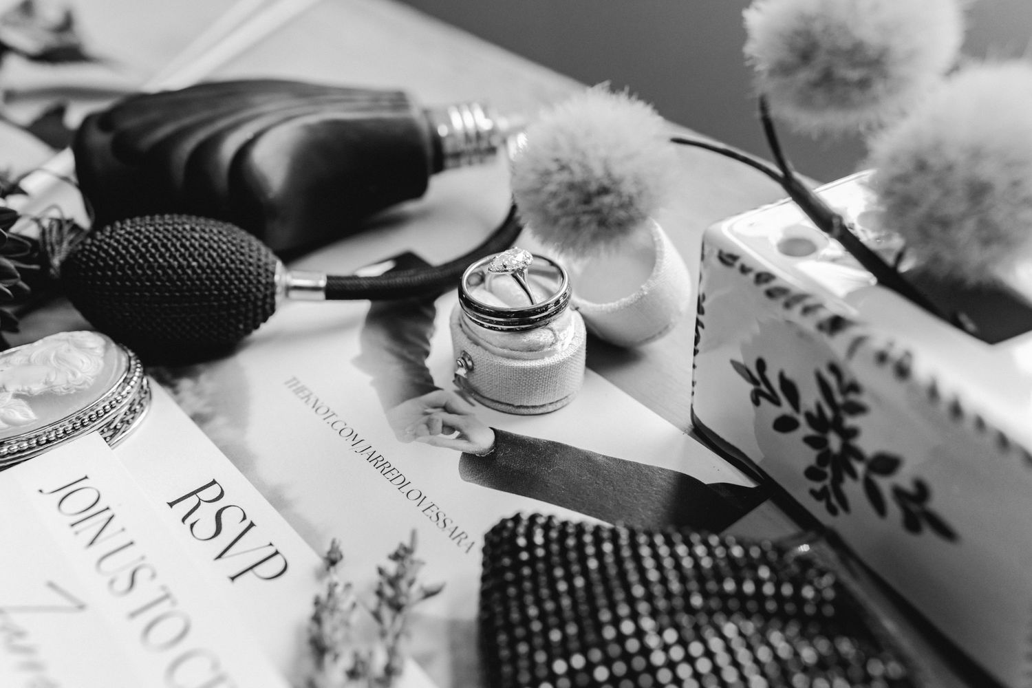 Black and white detail shot of wedding rings with cotton stems and perfume bottle.