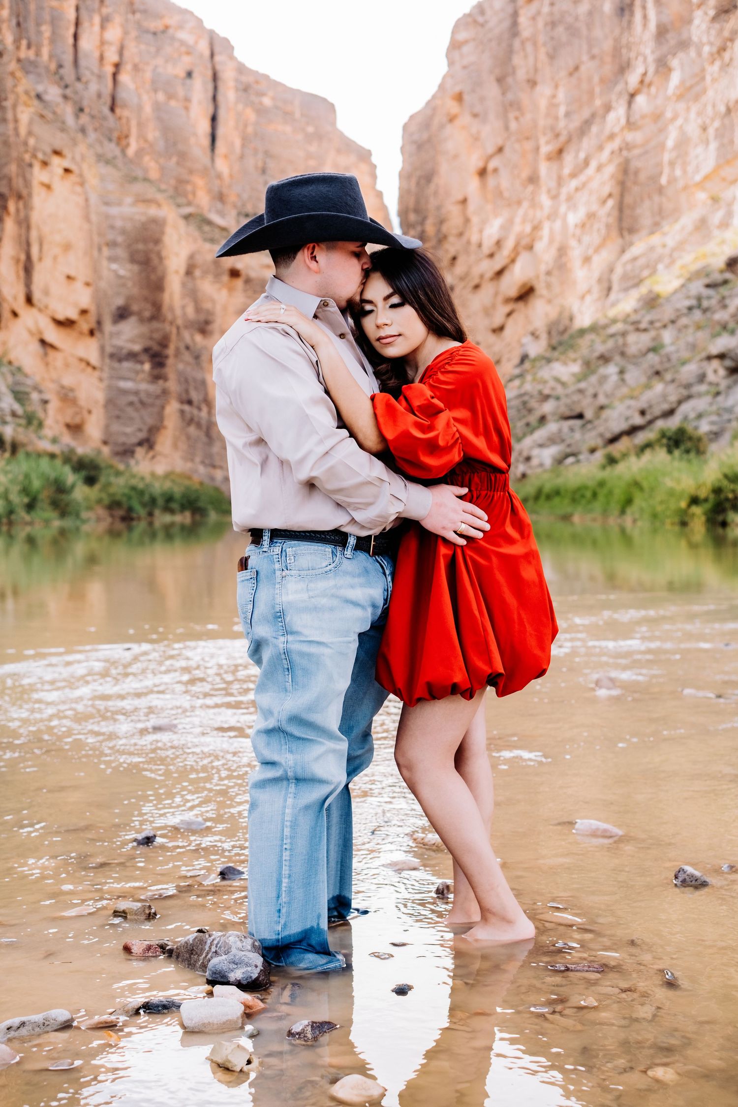 Intimate moment between couple in western wear standing in shallow canyon waters.