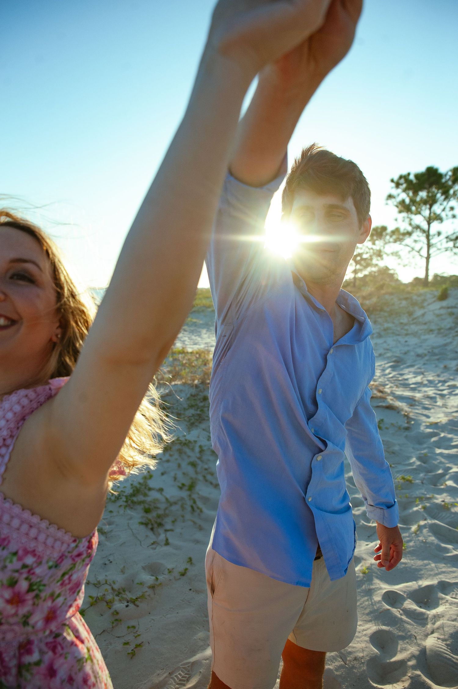 Playful beach photo with sun flare and couple dancing in summer attire.