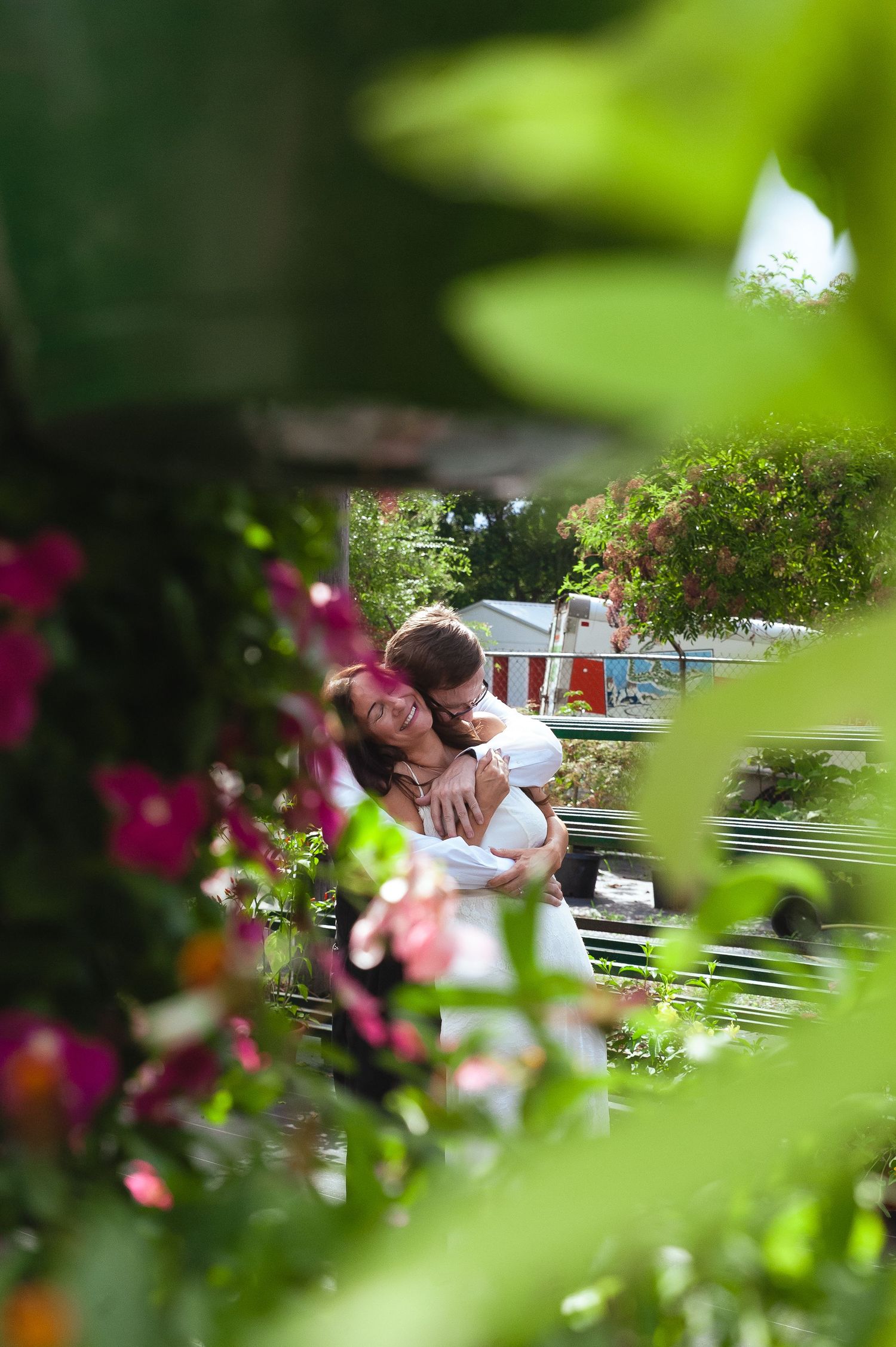 A romantic garden scene framed through blooming flowers and greenery showing tender moment on a sunny day.